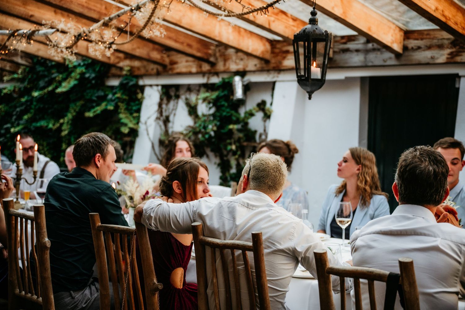 Wedding reception guests dining under wooden beams at an outdoor venue.