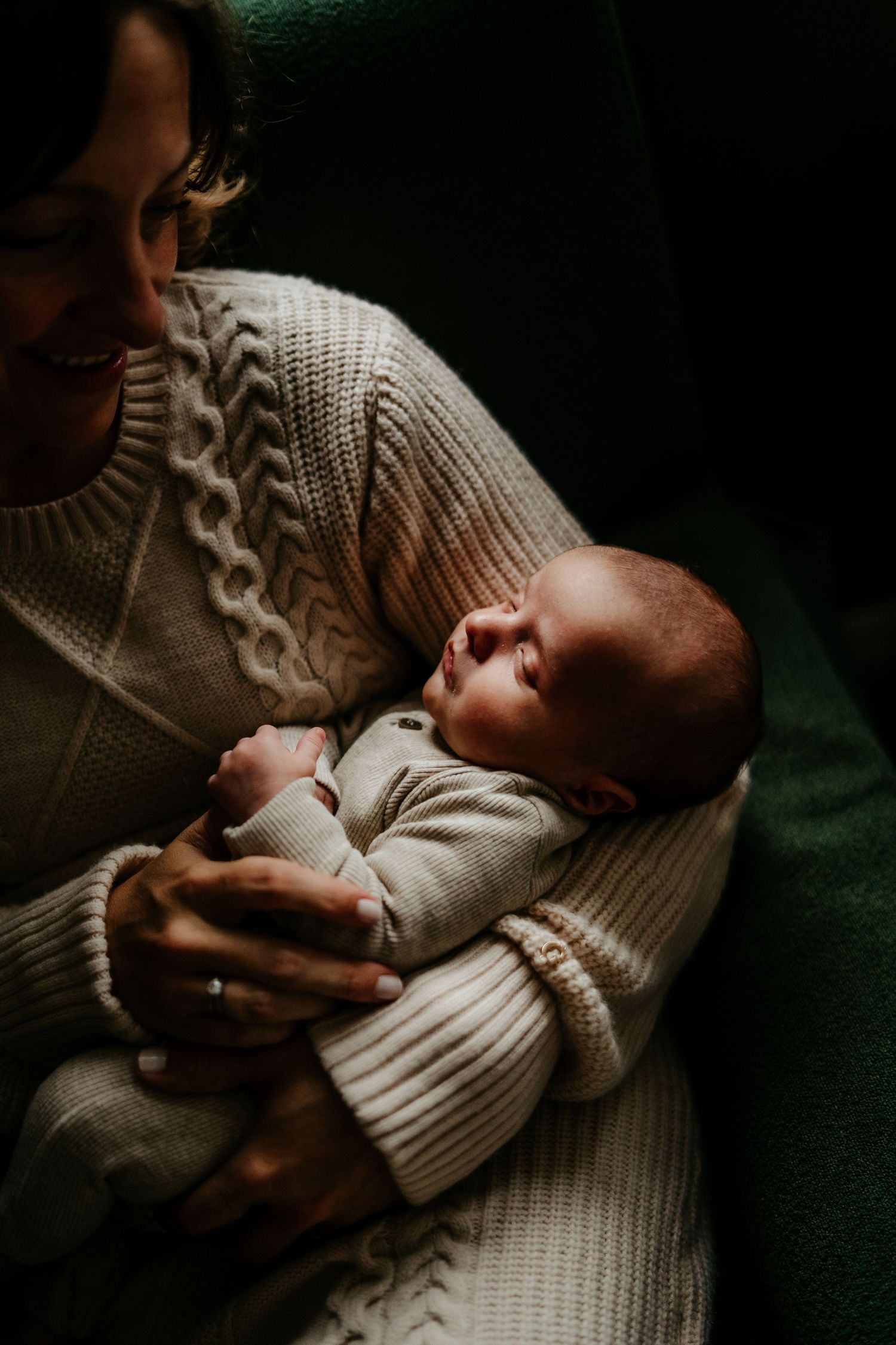 Close-up of mother cradling peaceful newborn baby in warm knit sweater.