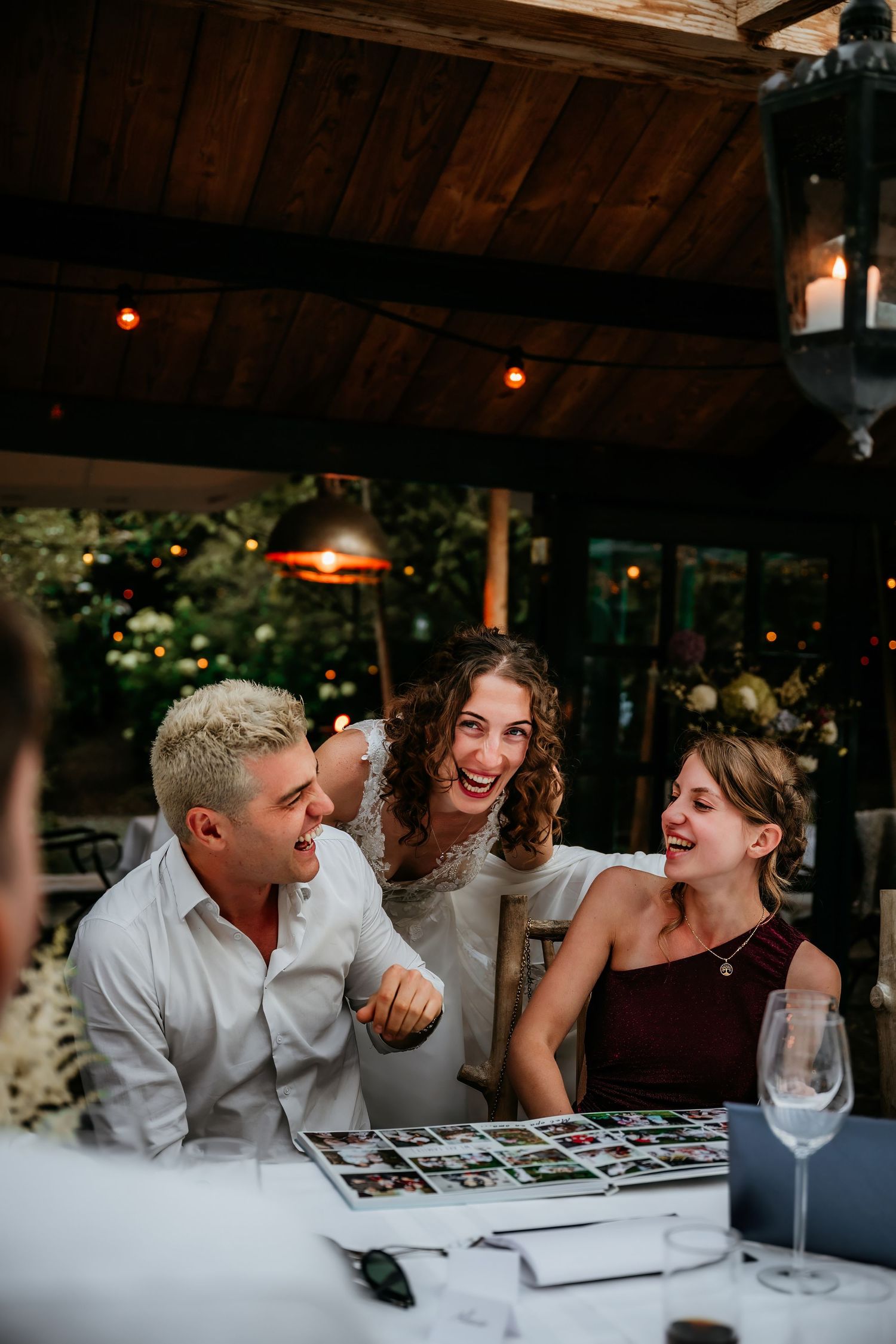 Wedding guests share laughter while signing the guest book under wooden beams at the reception.