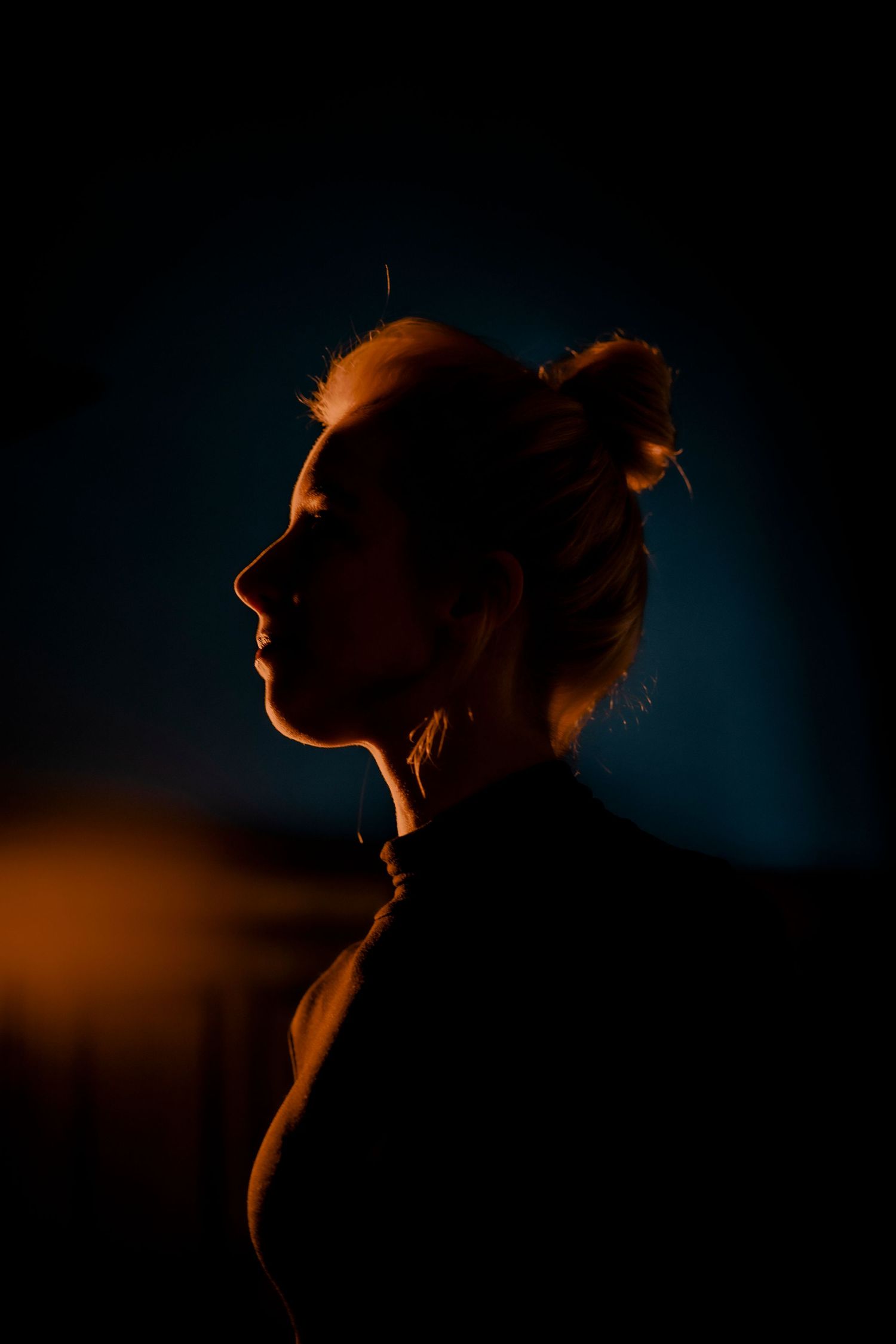 Dramatic silhouette portrait with orange rim lighting against dark blue background creates moody atmosphere.