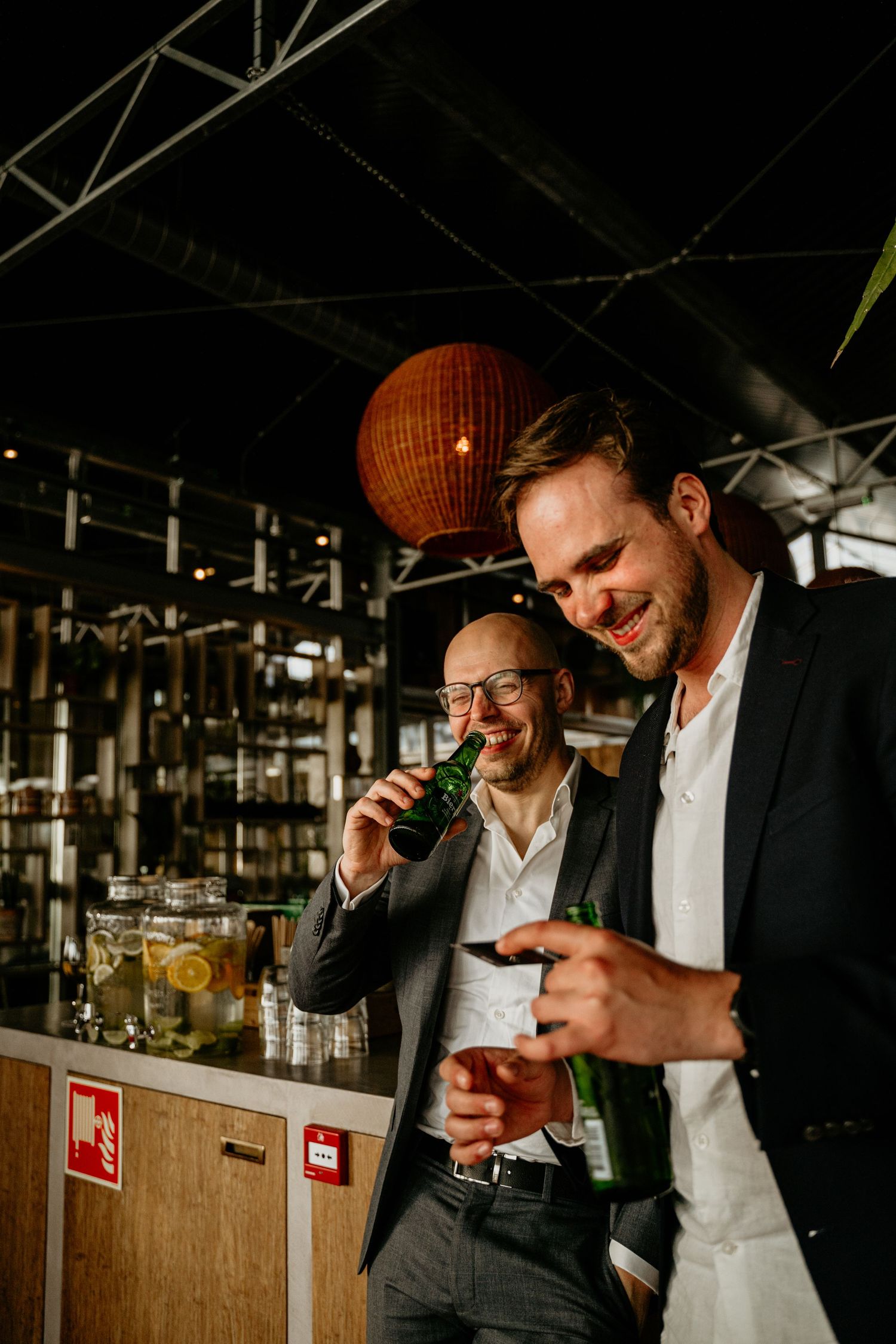 Men in suits sharing drinks and laughs at an indoor gathering.