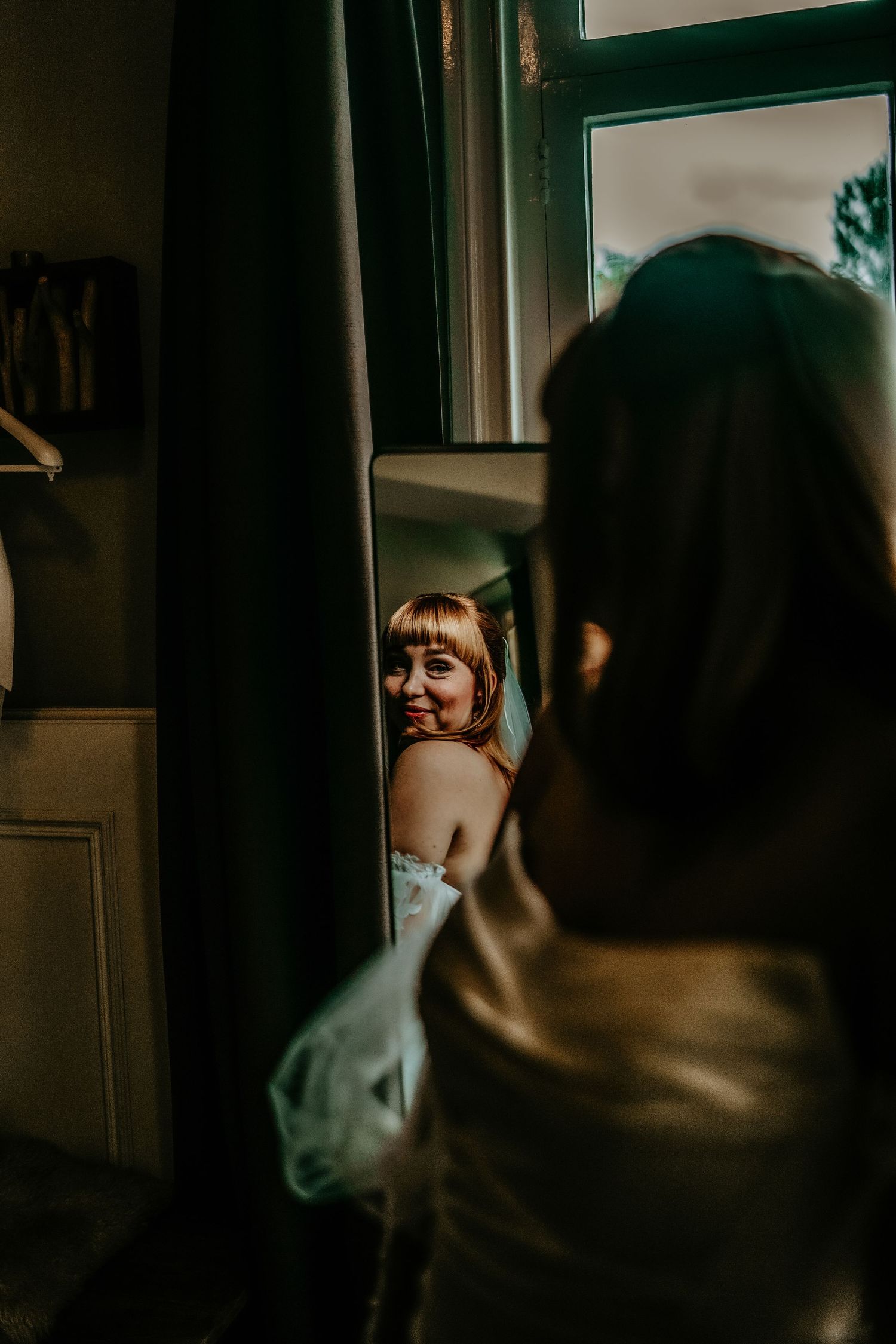A reflection in a mirror shows someone in a white dress getting ready in moody lighting.