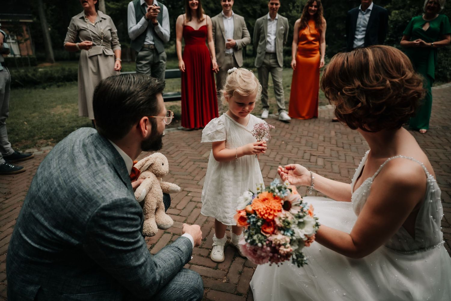 Wedding celebration scene with guests mingling outdoors on a brick patio during a sunny day.