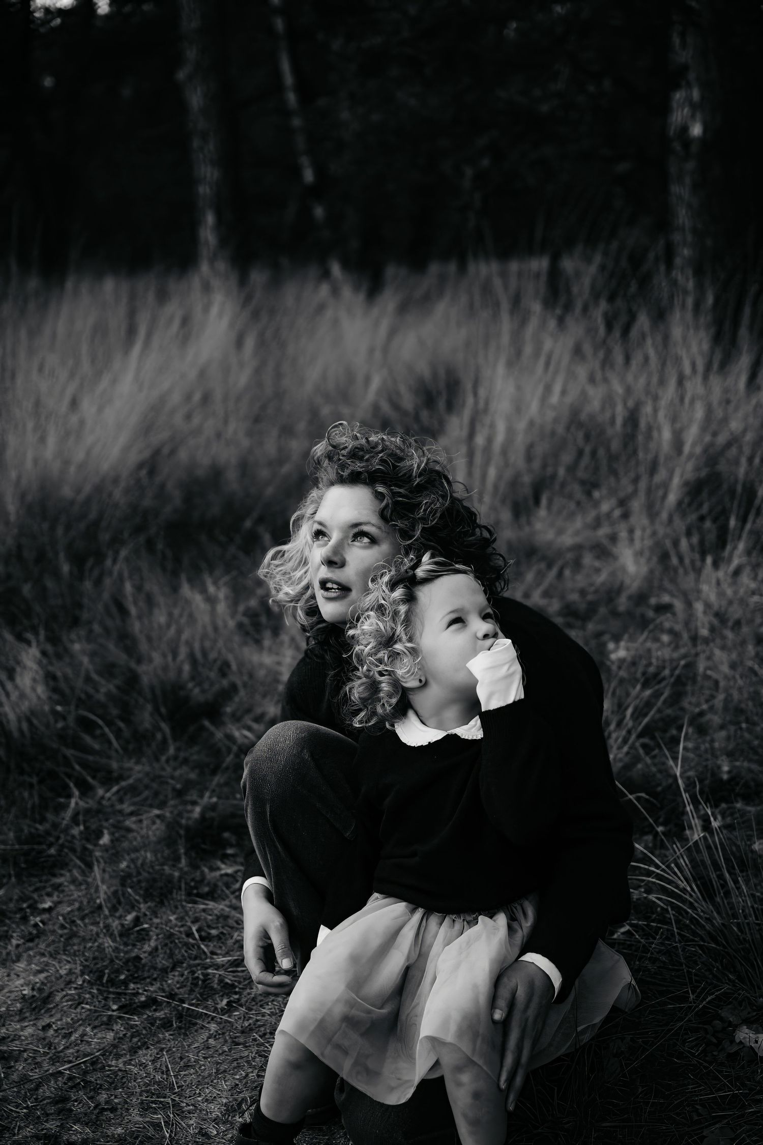 Artistic black and white portrait of two figures embracing in tall grass.