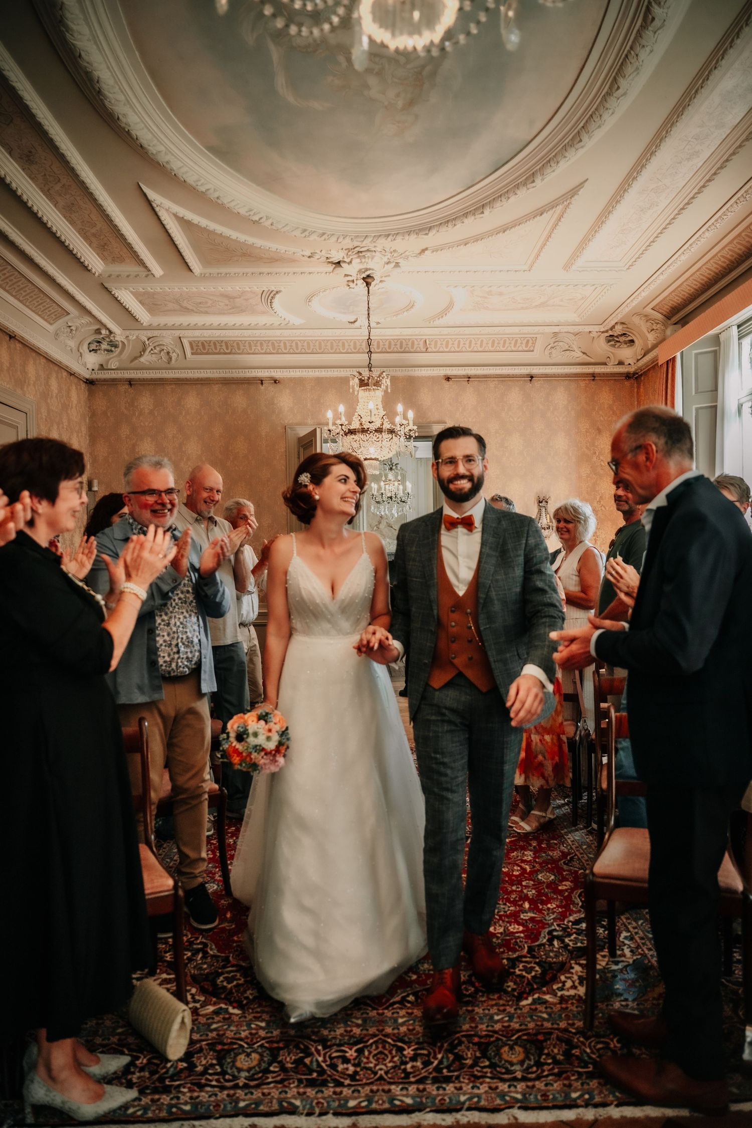Wedding celebration in an ornate room with decorative ceiling and chandelier.