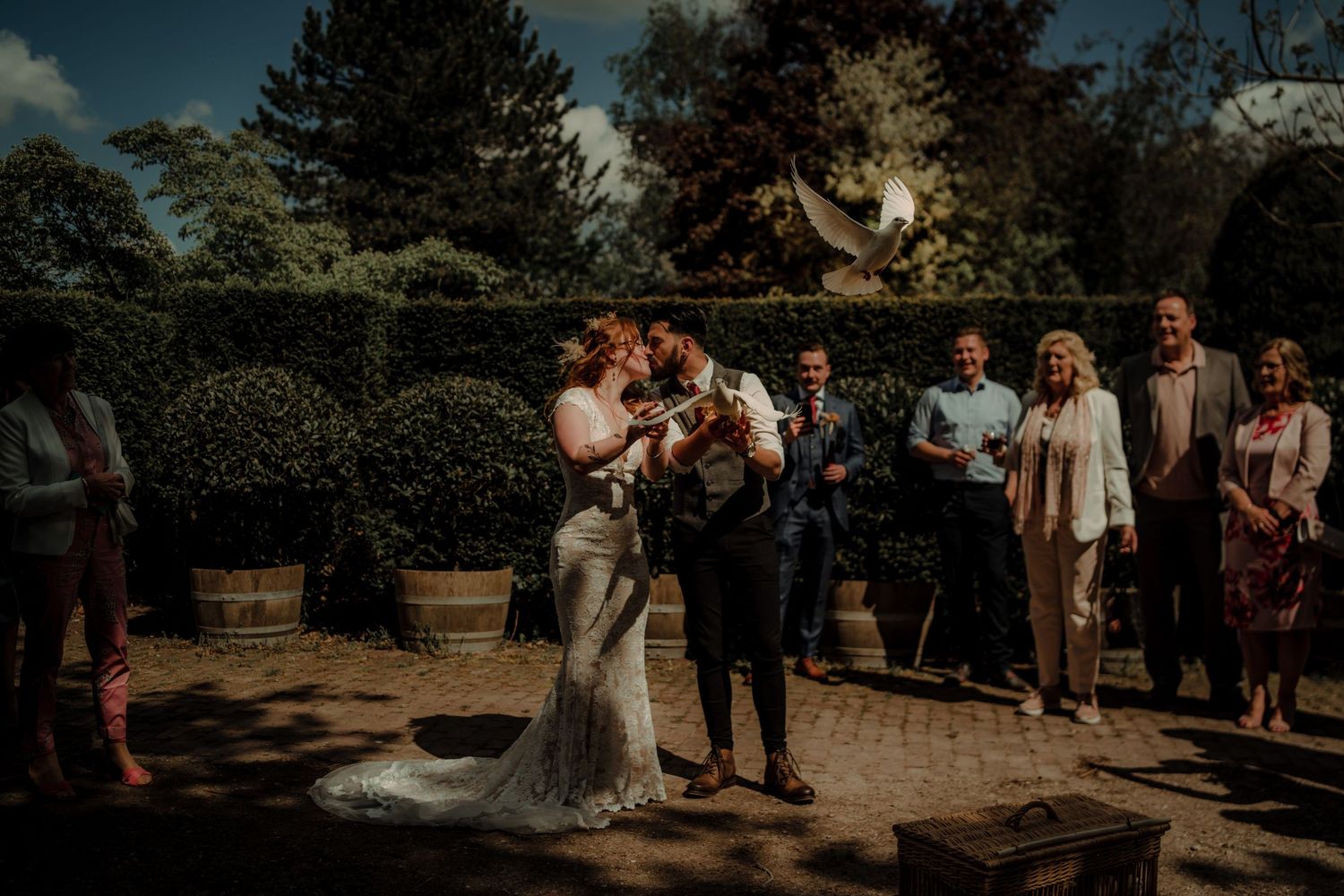 Outdoor wedding ceremony with guests gathered in garden setting at sunset.
