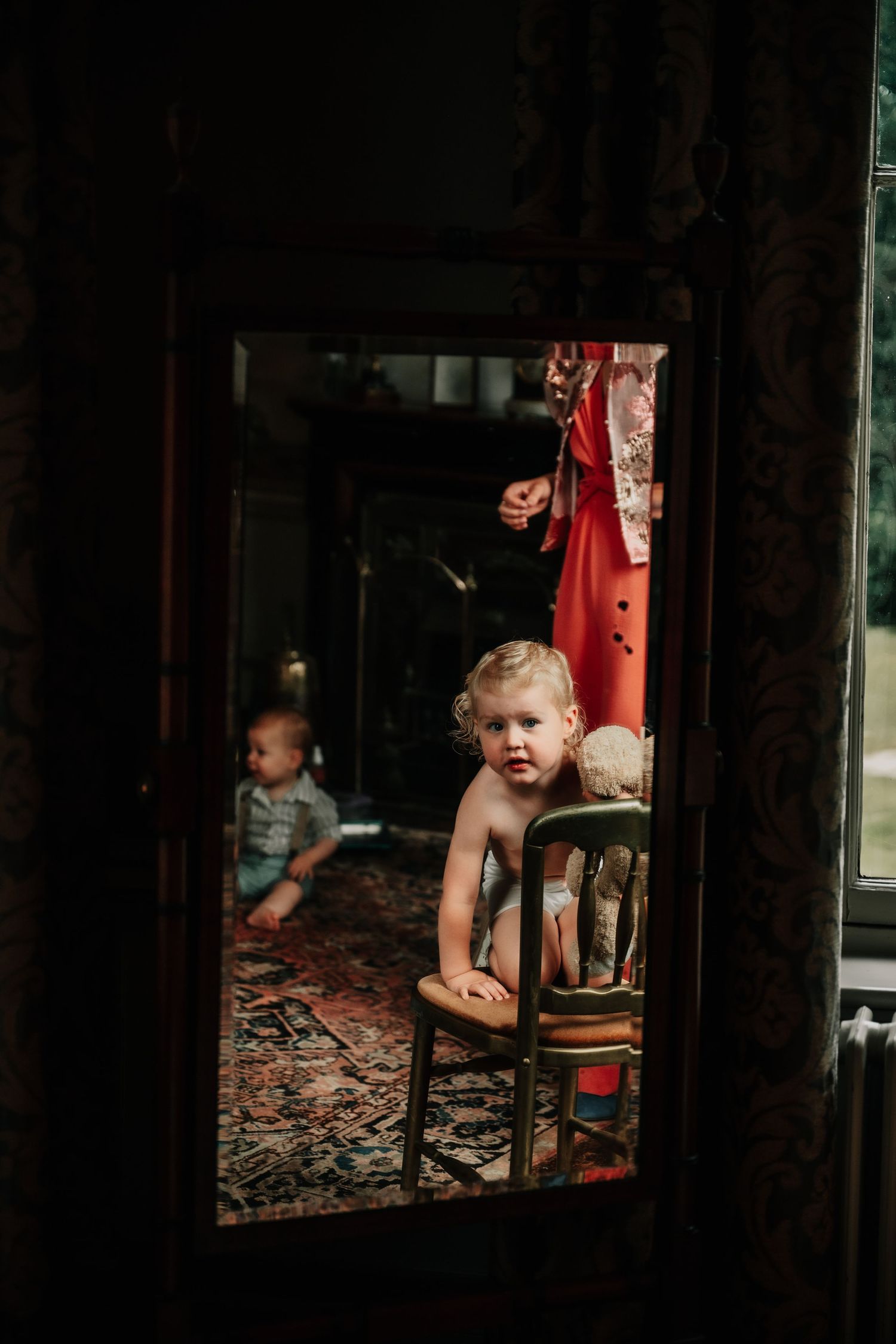 Moody interior scene with children visible through window reflections in dark lighting.