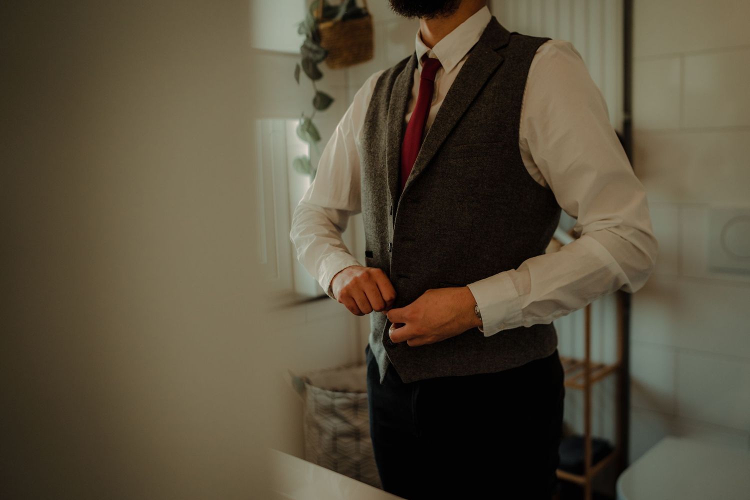 A person adjusts their formal attire while getting ready in a warmly lit room.