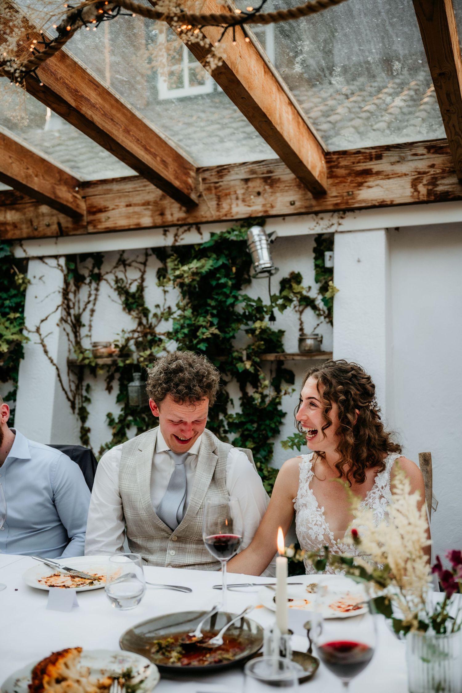 Wedding reception dinner under wooden beams with wine glasses and intimate table settings.