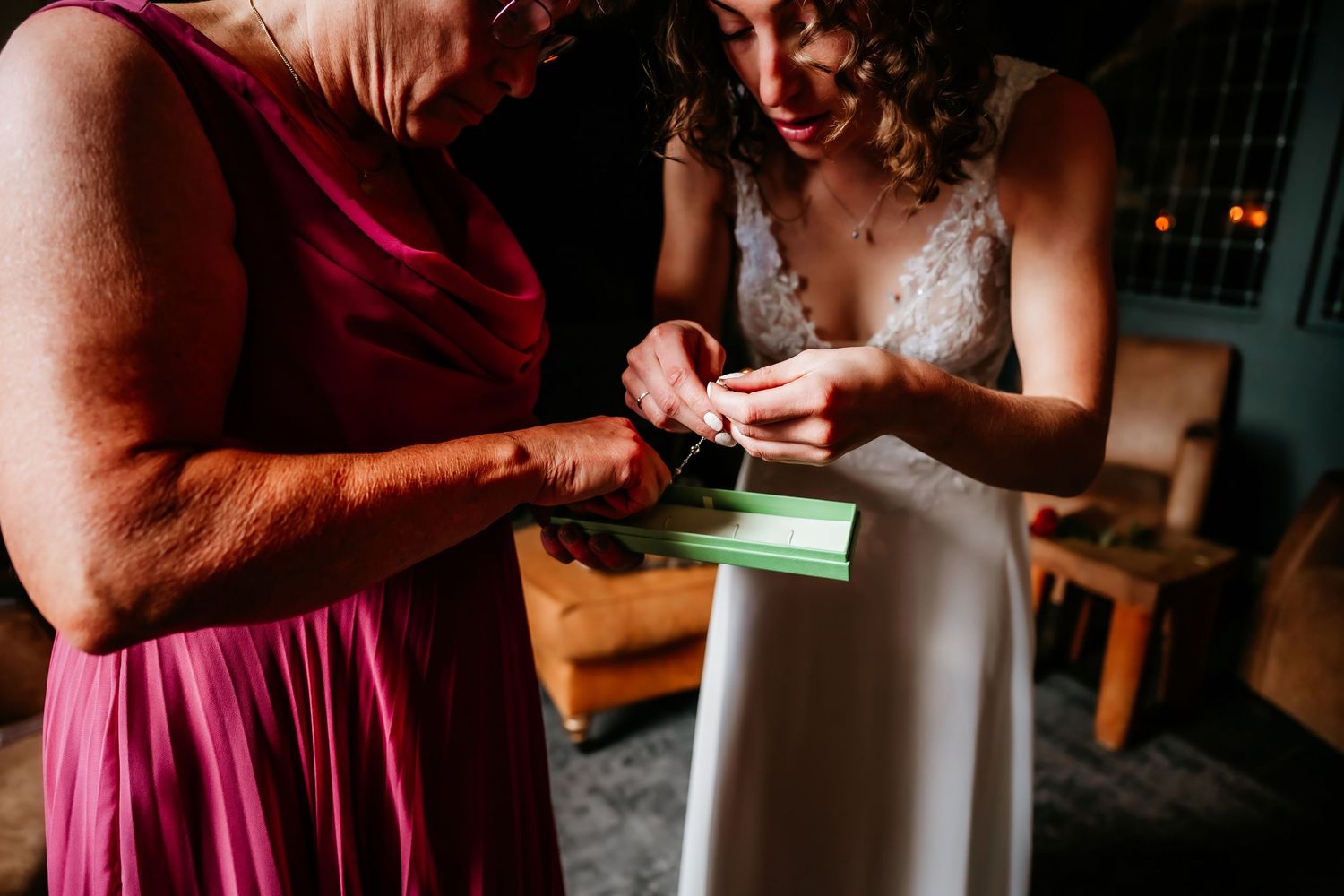Two people in formal dresses examine small items together in a dimly lit room.