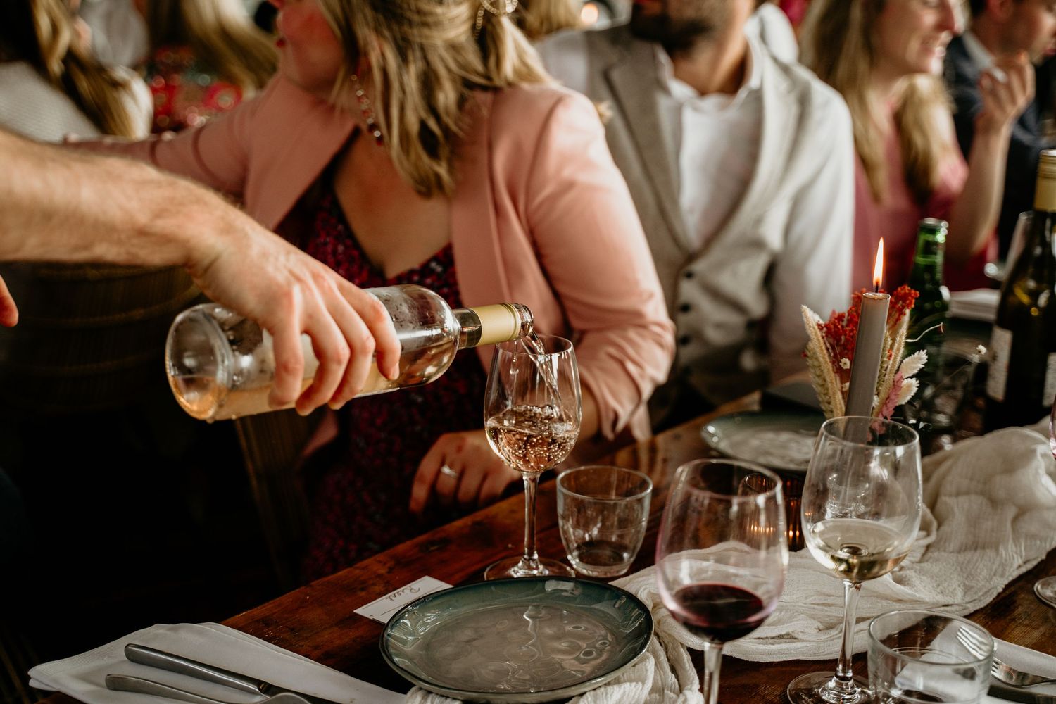 Someone pouring wine into glasses at an elegant dinner party.