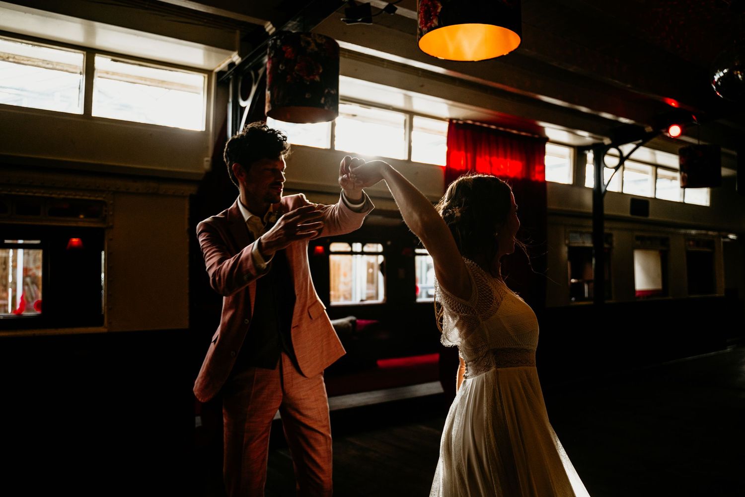 Silhouettes dancing in dimly lit room with orange lamp overhead.