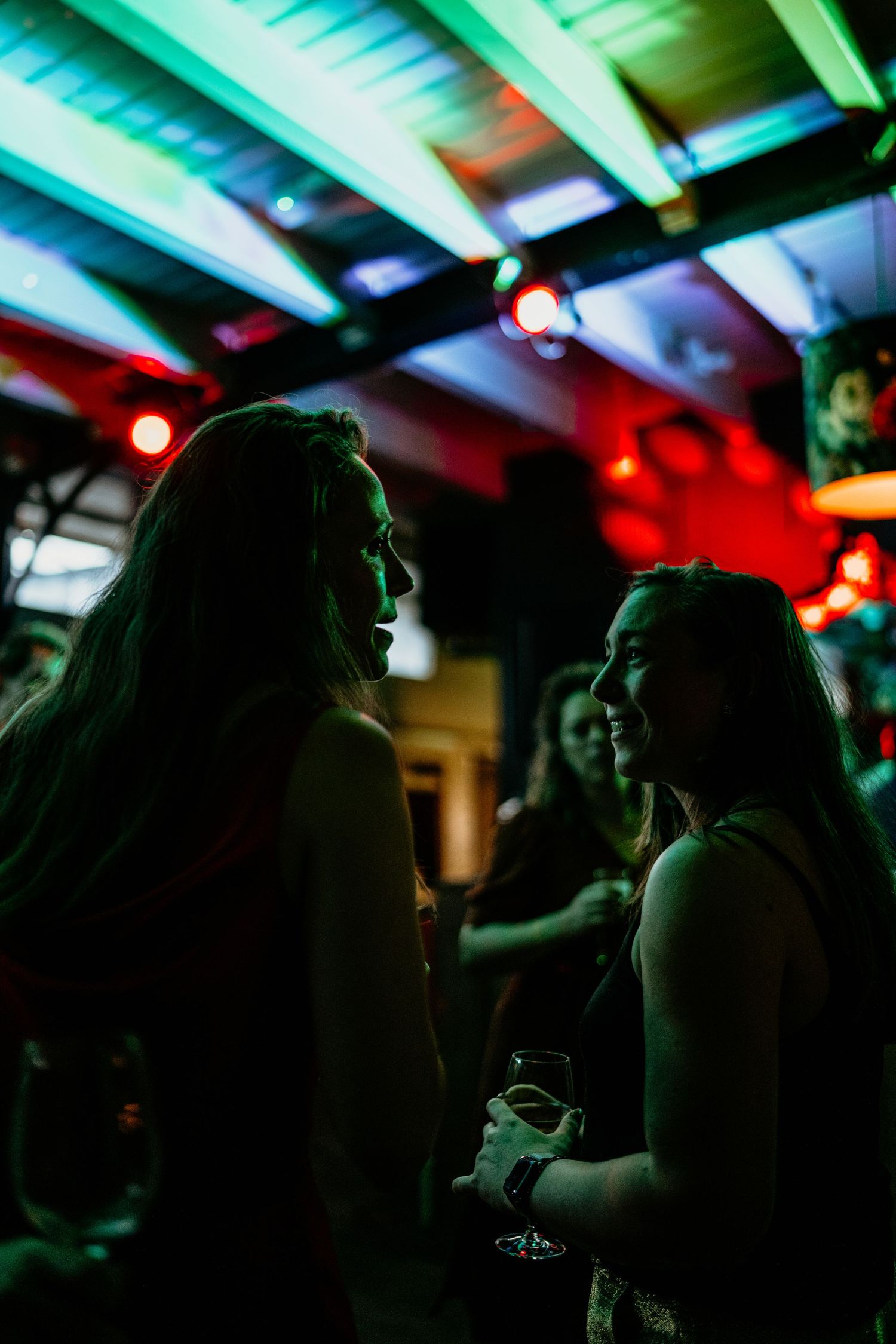 Silhouettes of party guests conversing under colorful mood lighting.