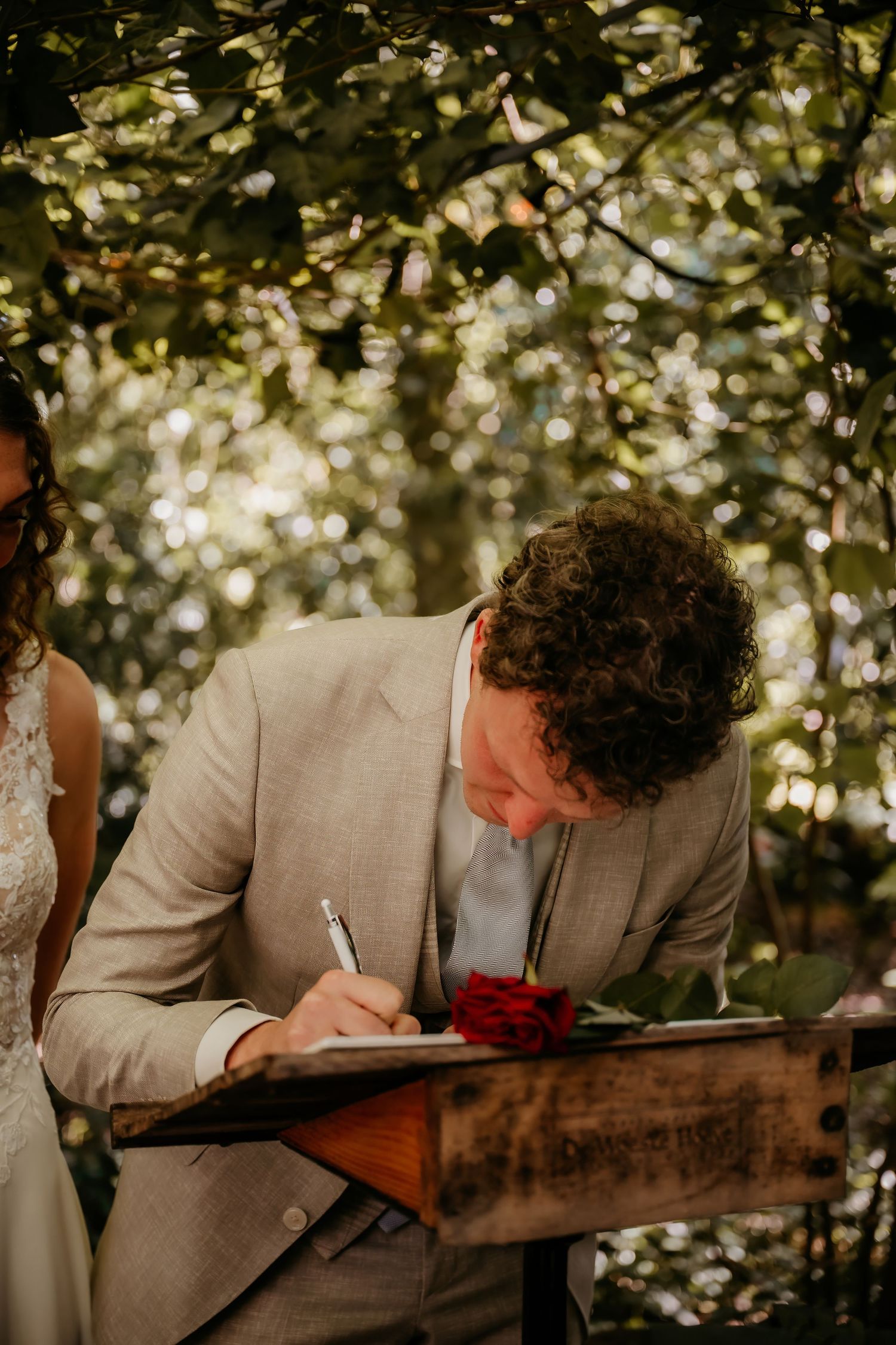 Someone signing documents at a rustic wooden table during an outdoor ceremony.