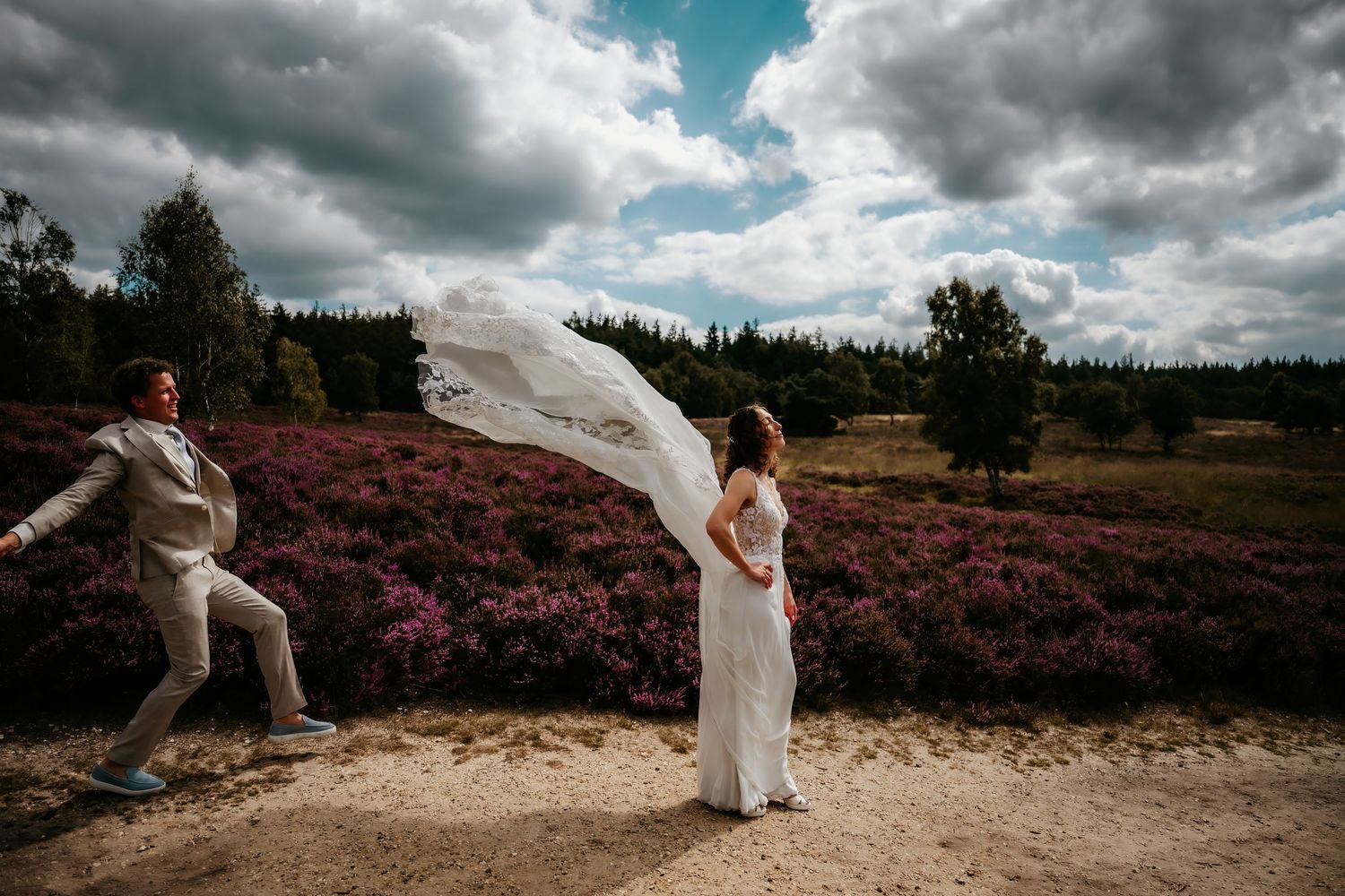 Wedding couple poses dramatically against a purple heather field under dramatic cloudy skies.