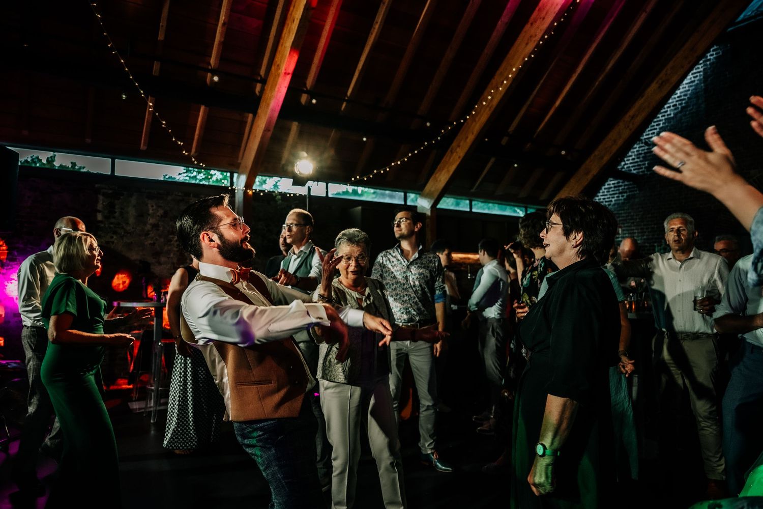 Wedding guests dance and celebrate on a dimly lit dance floor.