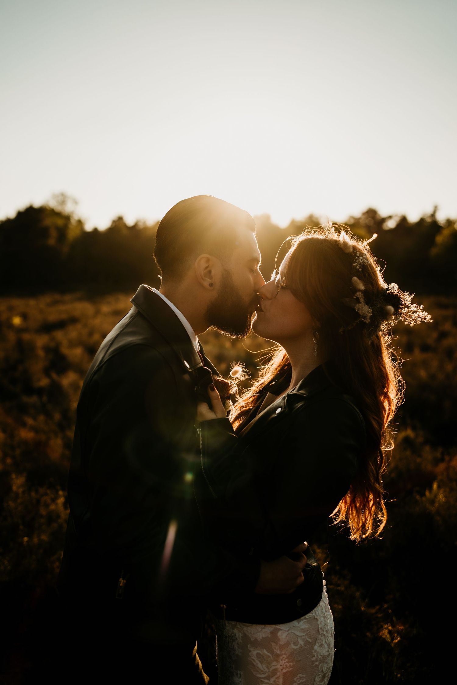Silhouetted newlyweds sharing a tender kiss in warm sunset lighting.
