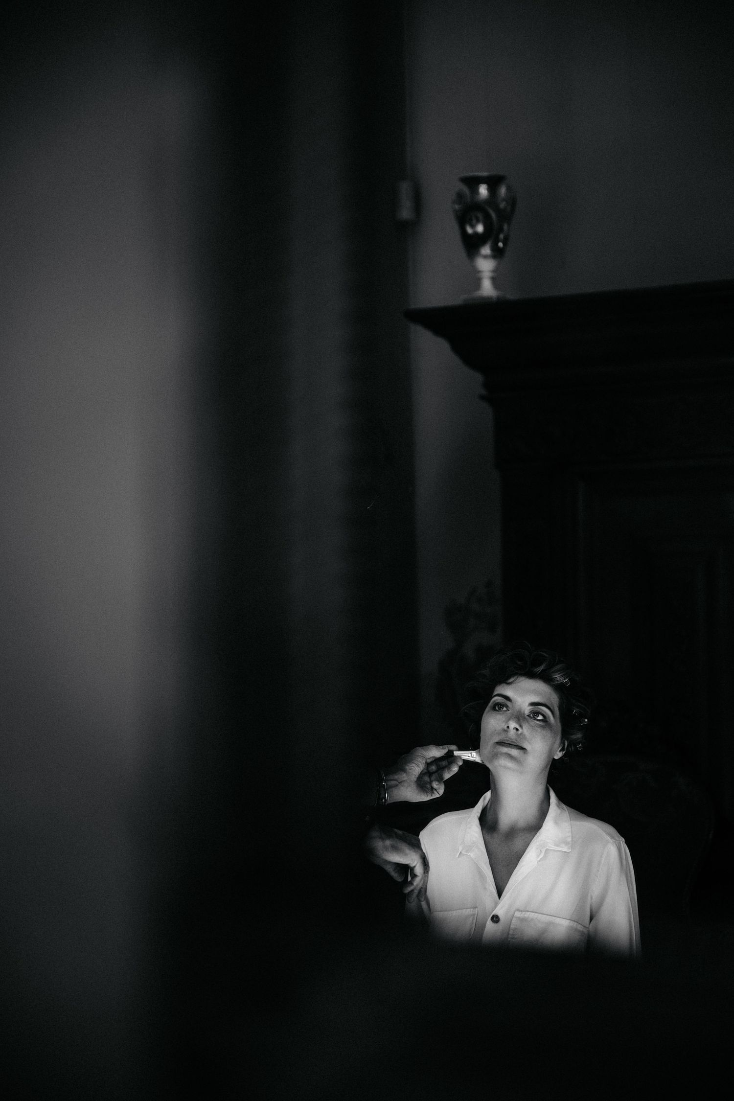 Dramatic black and white portrait of someone smoking in low light with a vase silhouetted in the background.
