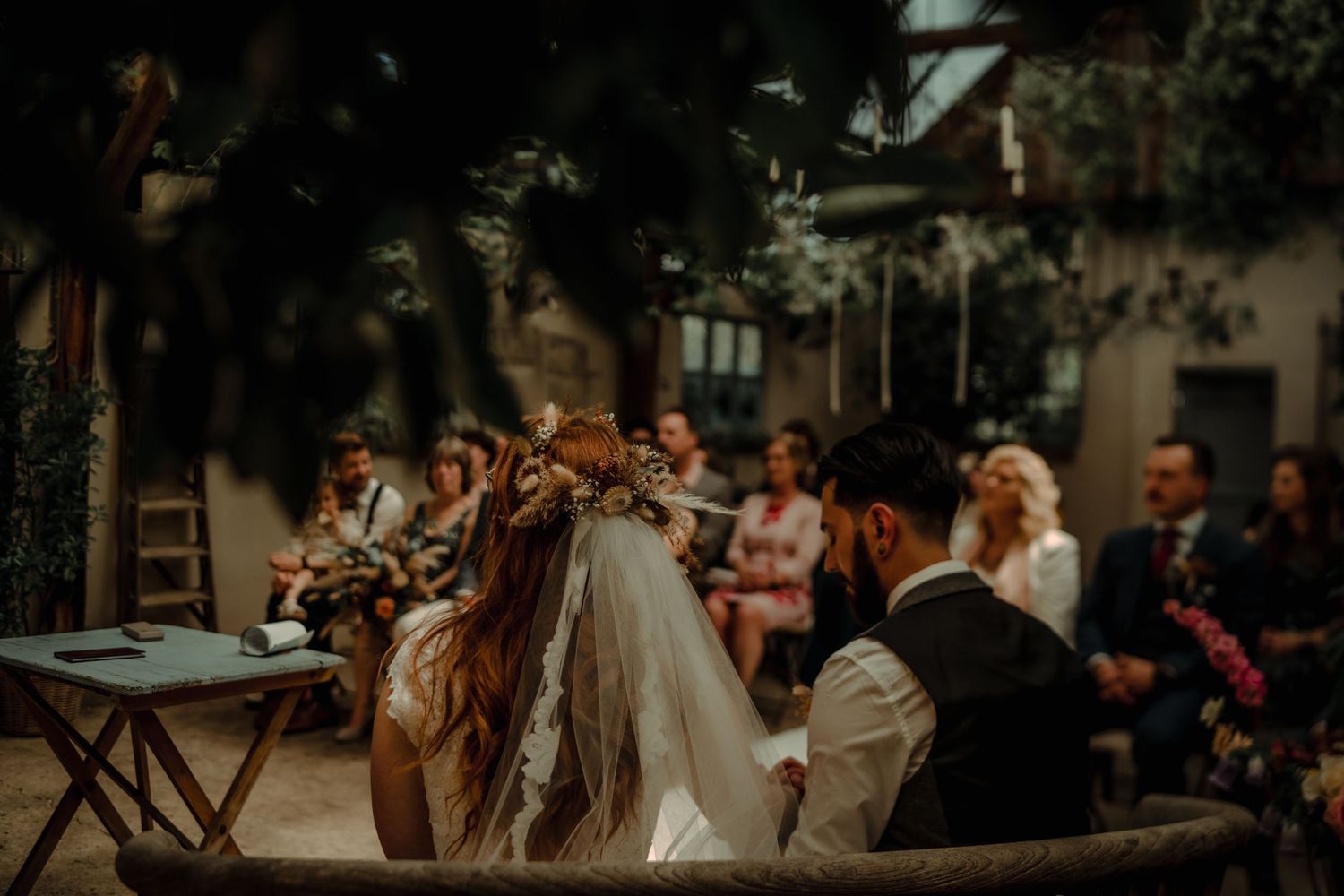 Wedding guests seated at outdoor ceremony with dappled sunlight through trees.