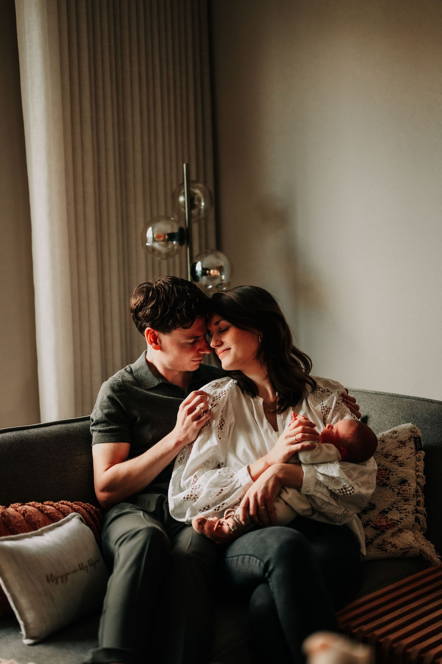 An intimate family moment on a grey couch beneath hanging pendant lights.