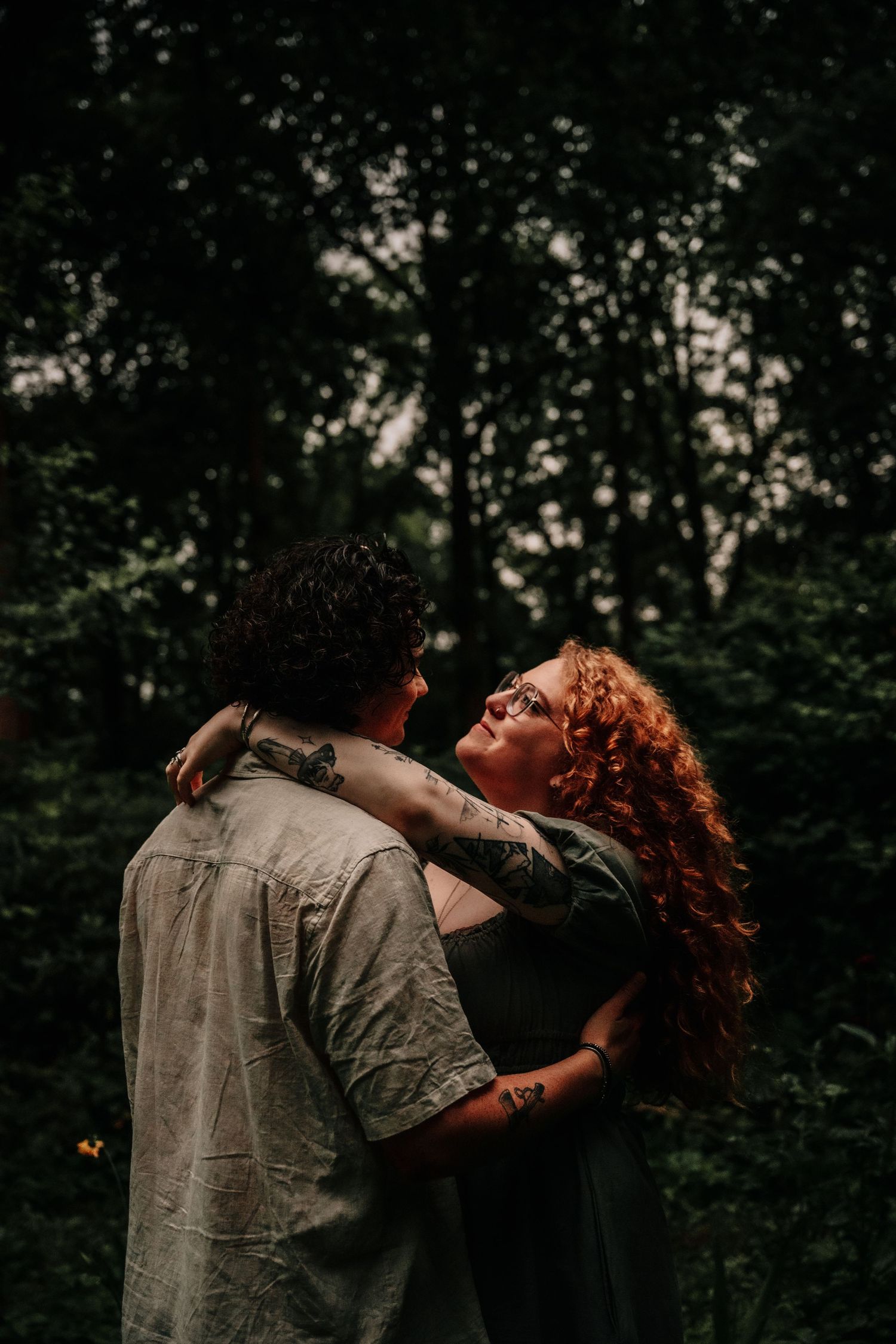 A couple embraces intimately in a dark wooded setting, with soft lighting illuminating their romantic moment.