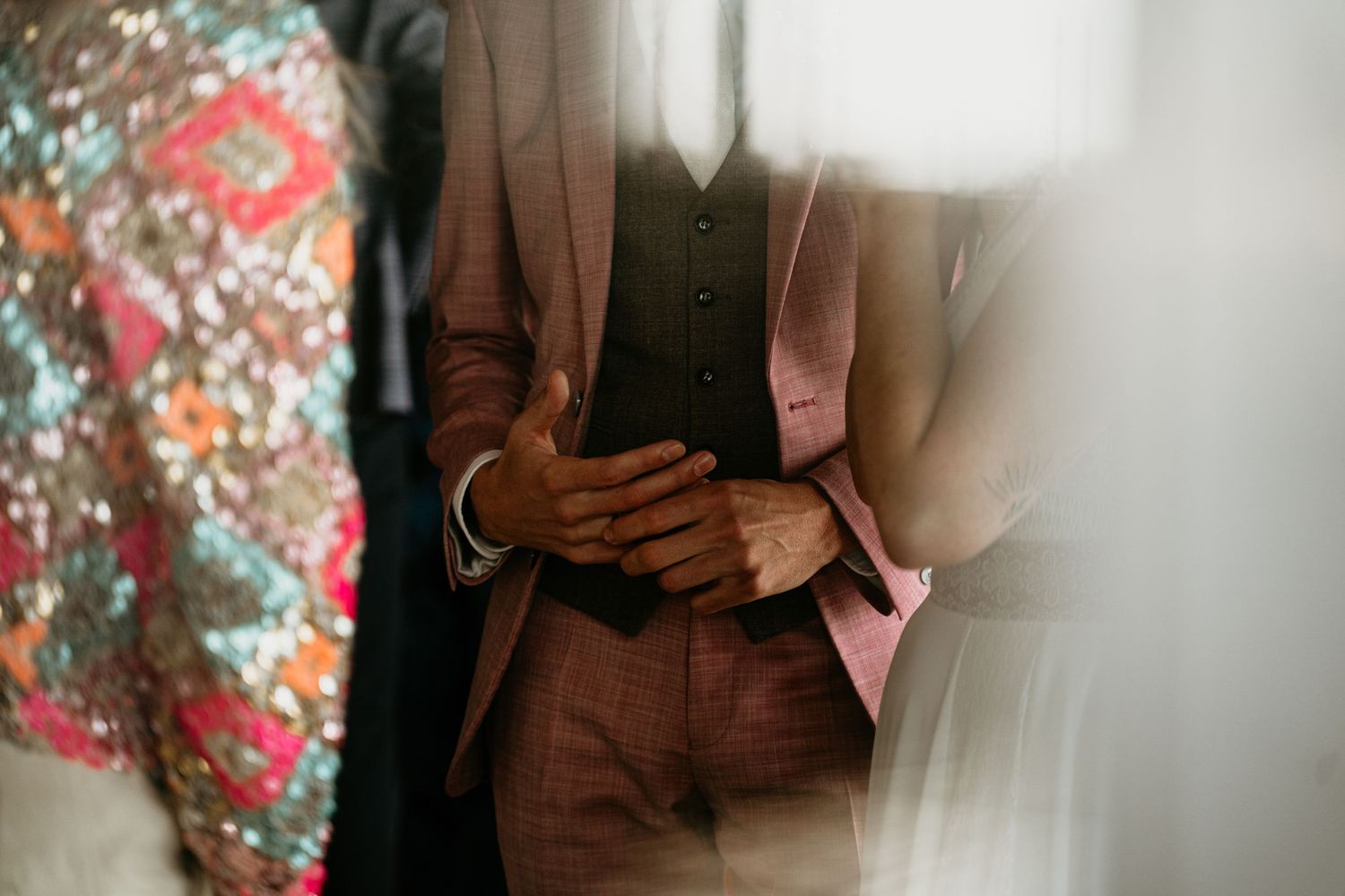 A wedding couple poses in formal attire against a floral backdrop with soft lighting.