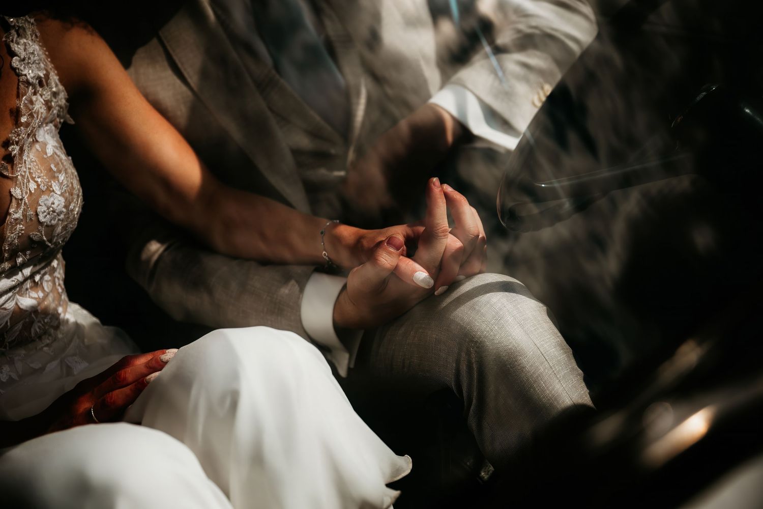 Close-up shot of wedding couple's hands touching tenderly in moody lighting.