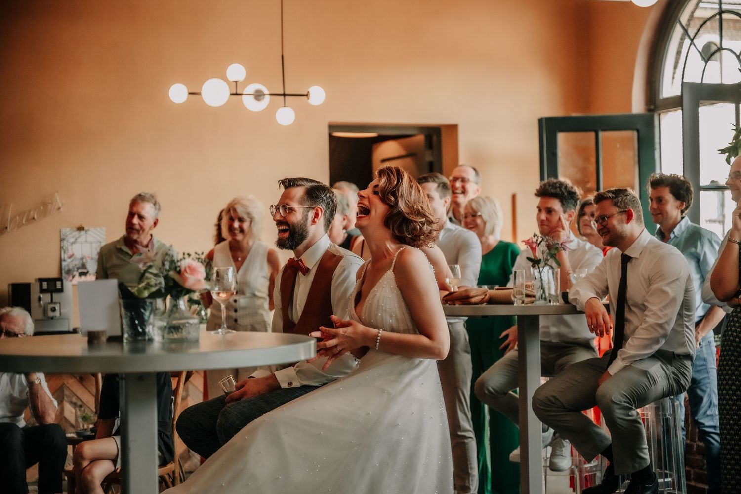 Wedding reception scene with guests seated at tables in warm natural lighting.