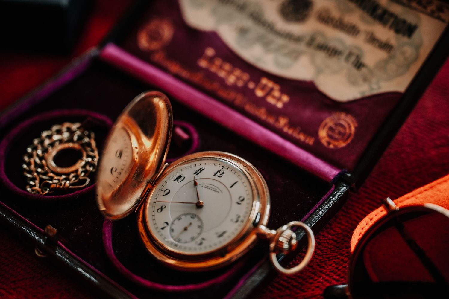 Vintage pocket watches and timepieces arranged on a dark red velvet surface in moody lighting.