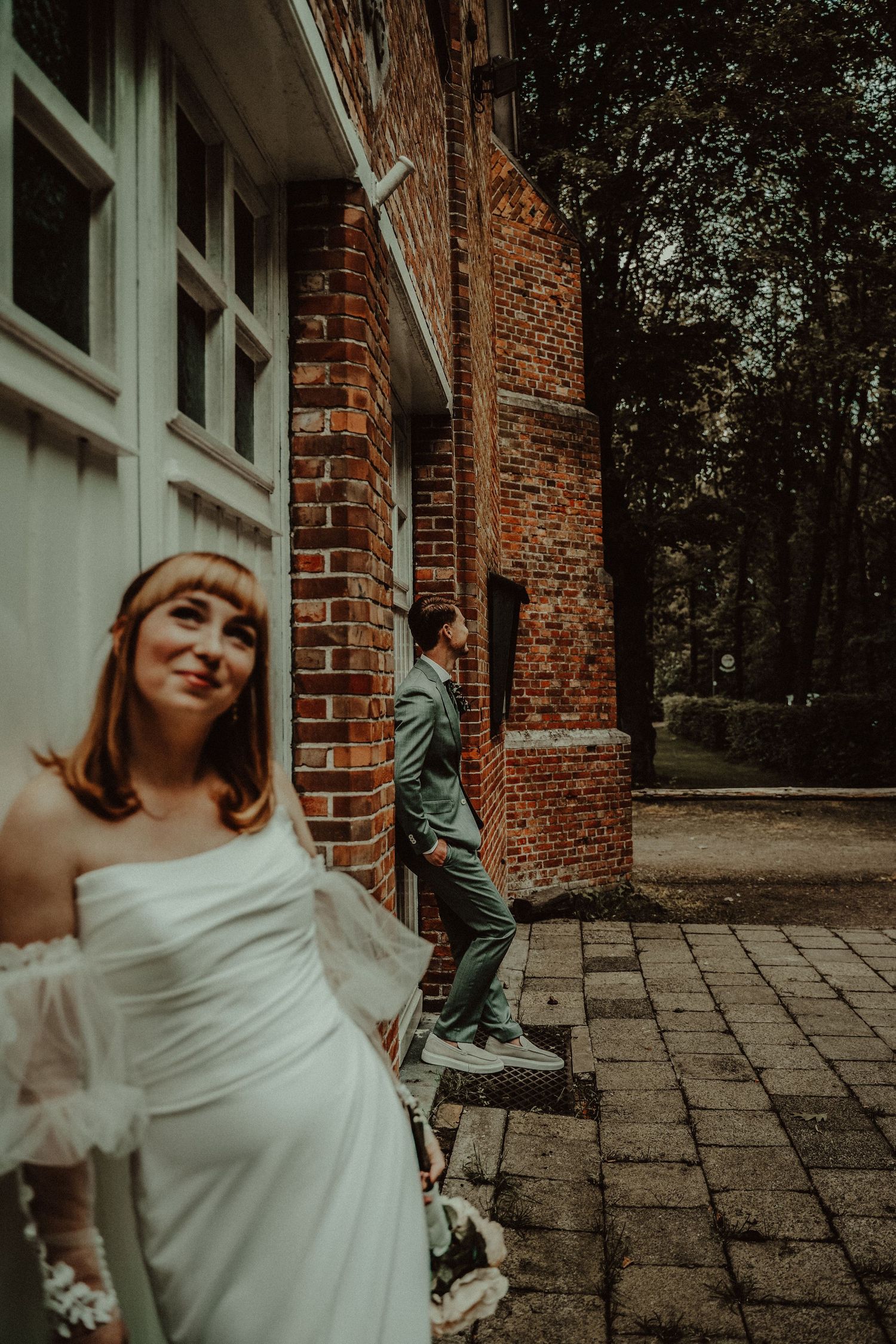 A couple poses playfully outside a brick building during their wedding photoshoot.