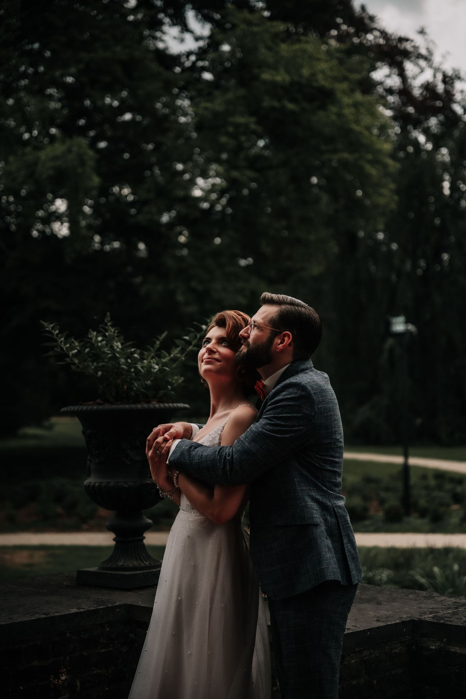 Romantic moment captured against a dark outdoor garden setting with stone urns.