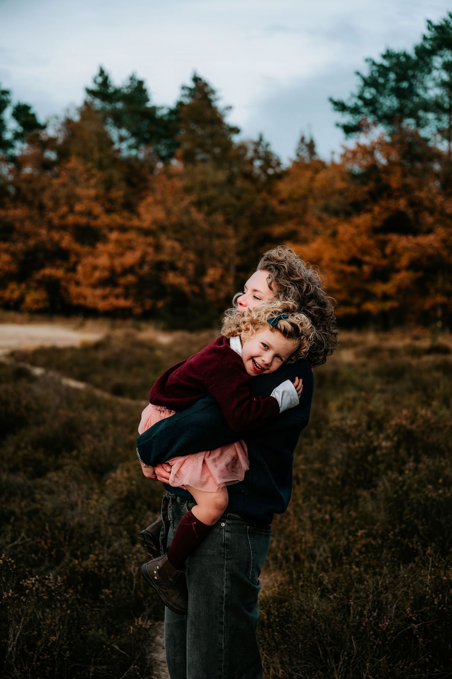 Two people share a joyful embrace in an autumn field with orange trees in the background.