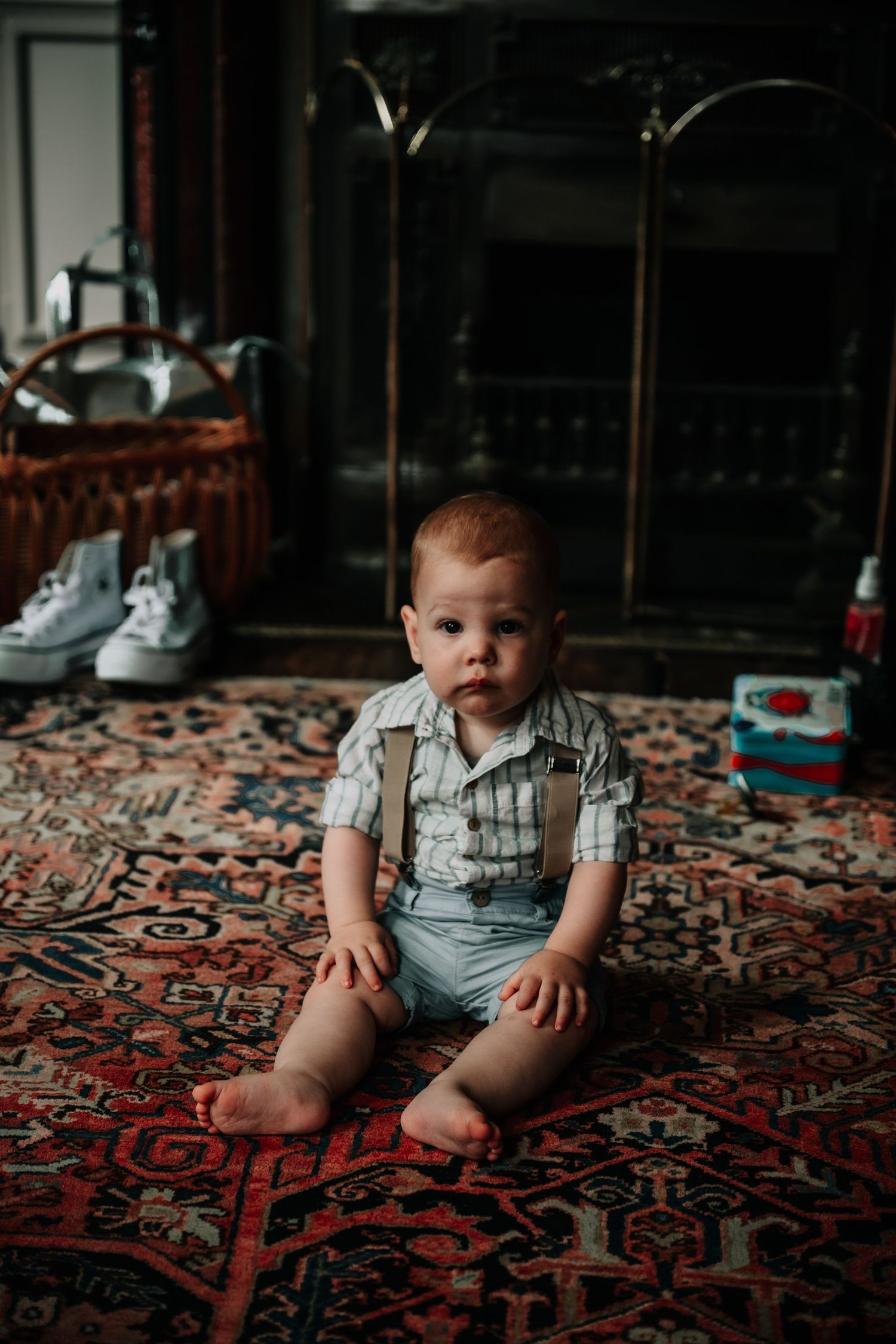 Small child sits on an ornate patterned carpet in a dimly lit room wearing casual clothing.