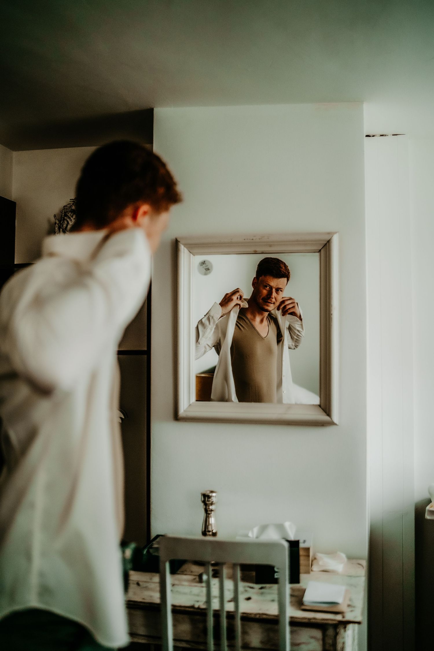 Mirror reflection showing wedding day preparations in minimalist room setting.