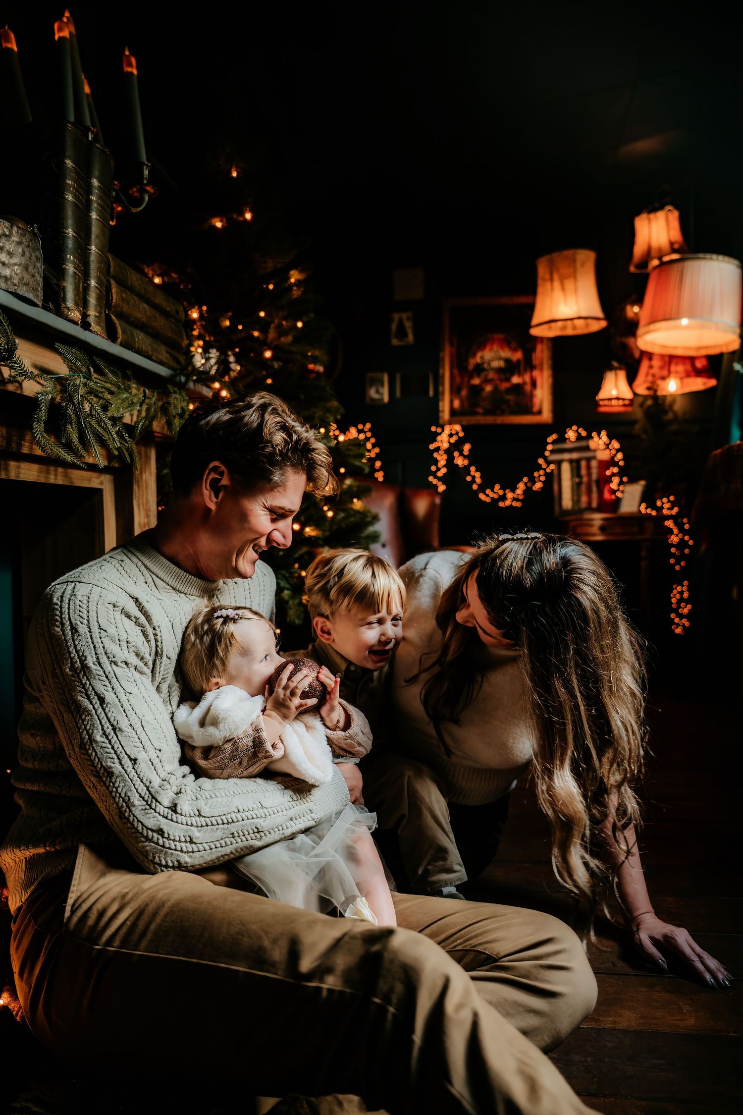 A family shares tender moments together on a couch in a dimly lit room with warm ambient lighting and string lights.