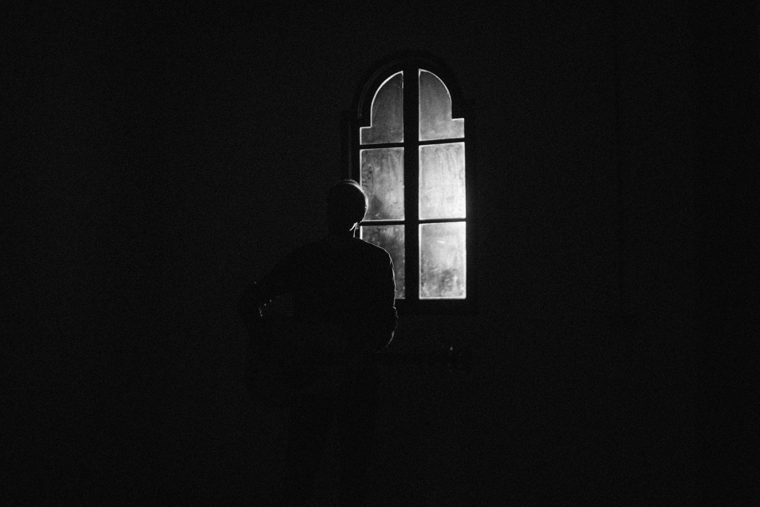 A dramatic black and white architectural photograph shows light streaming through a window in darkness.