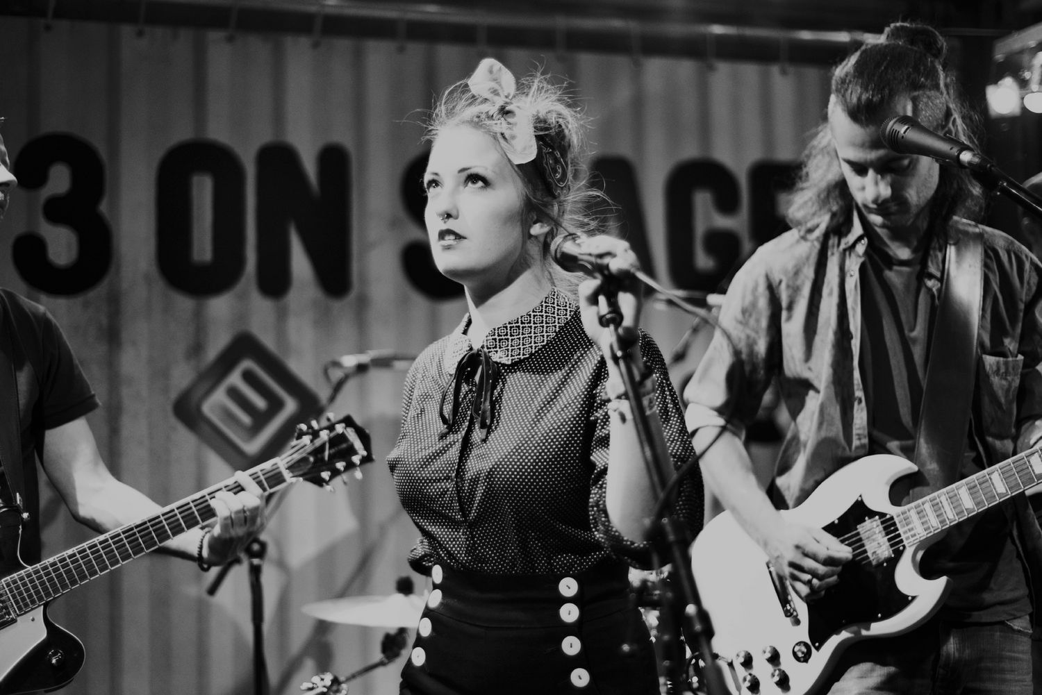 Black and white photo of a rock band performing on stage with guitars and intense lighting effects.