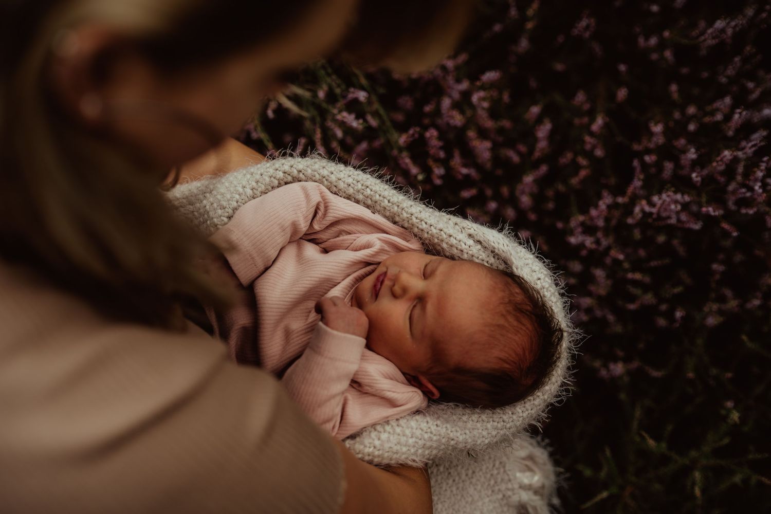 Newborn baby wrapped in knit blanket smiles during lifestyle photo session.