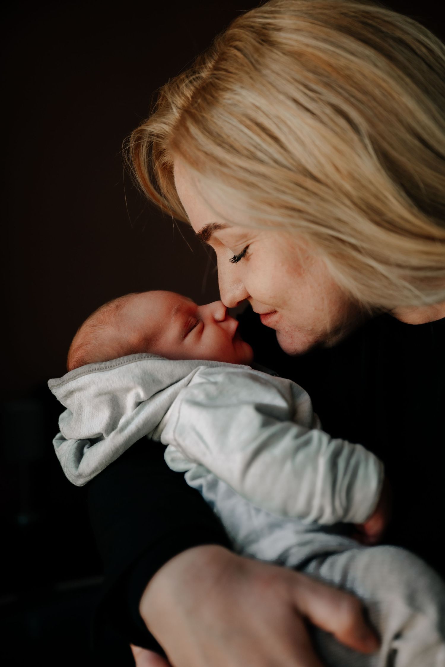 Intimate bonding moment between mother and baby in moody lighting.