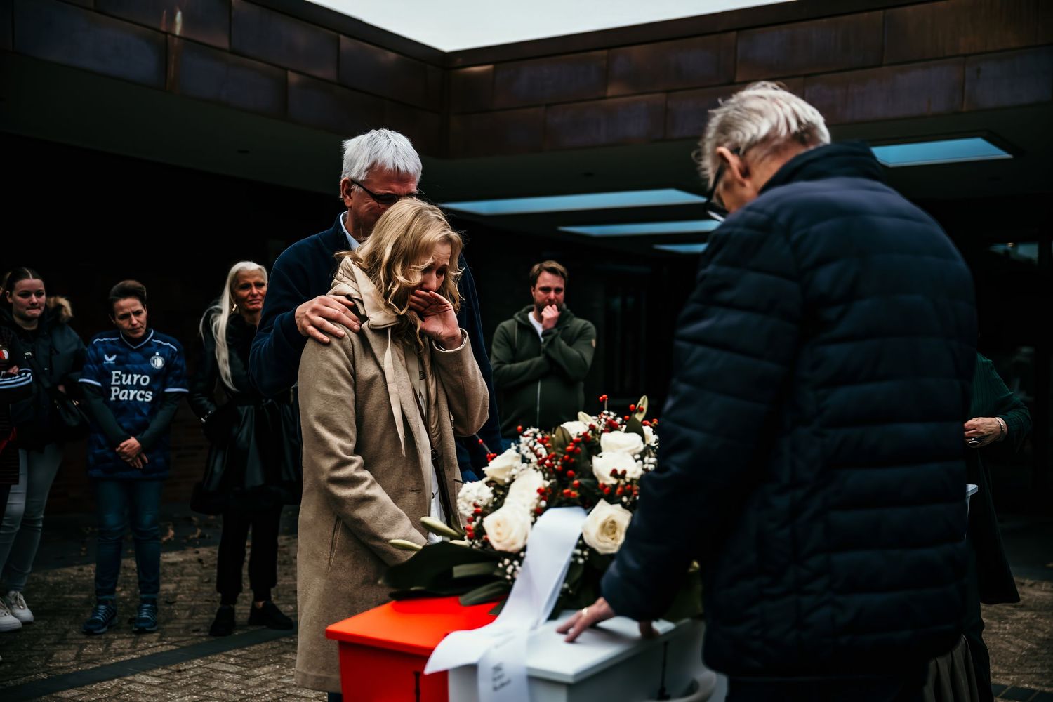 A group of people gather outdoors around a small red platform during a winter ceremony.