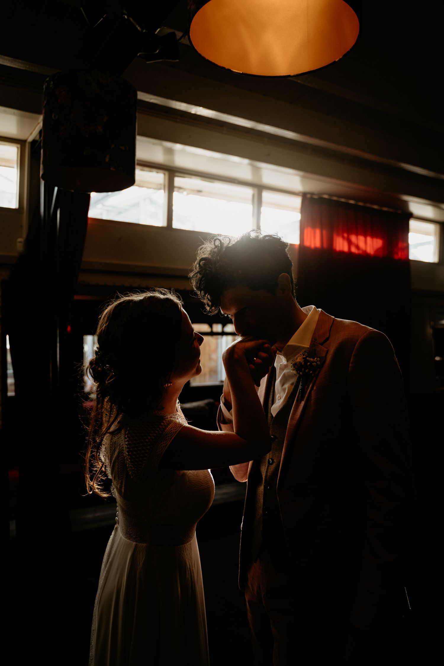A silhouetted couple shares an intimate dance moment under warm lighting in a reception venue.