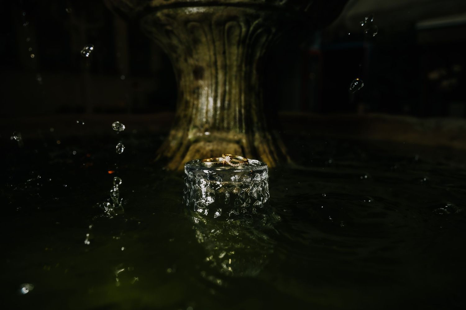 Close-up of a decorative stone fountain with water splashing at its base in a dark outdoor setting.