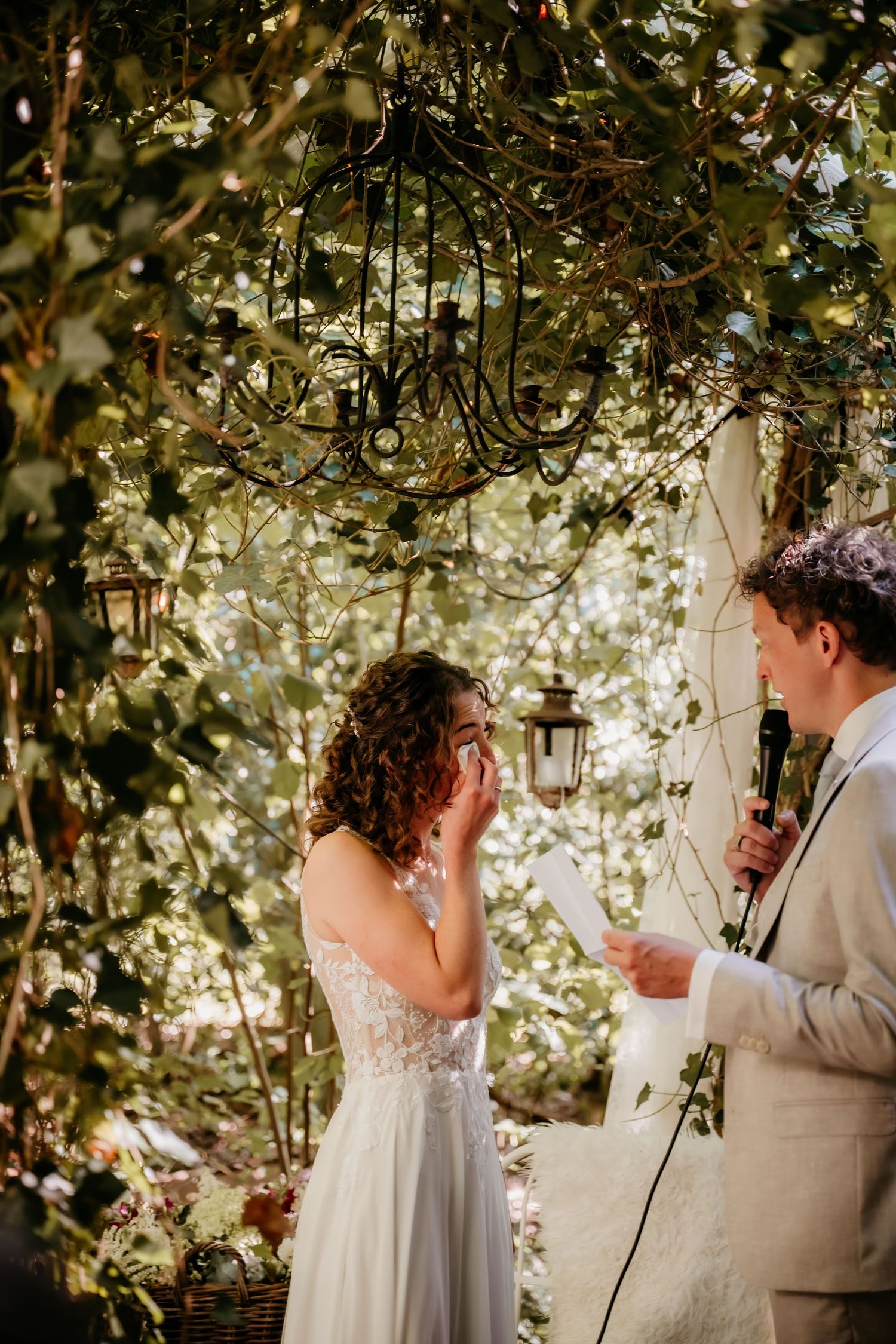 Wedding couple exchanges heartfelt vows under a natural arbor decorated with hanging lanterns.