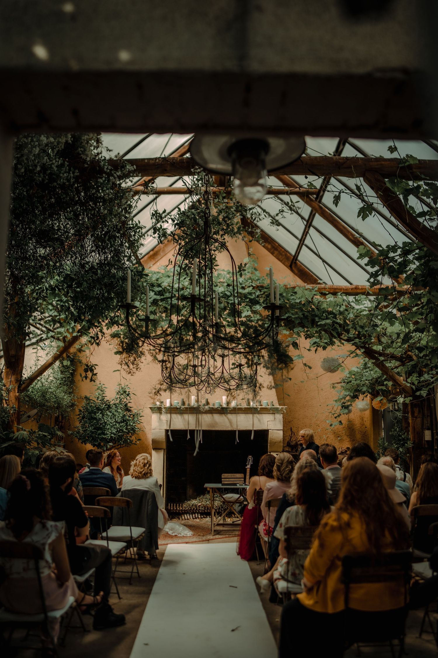 Wedding reception venue with rustic greenhouse setting and natural light filtering through glass panels during sunset.