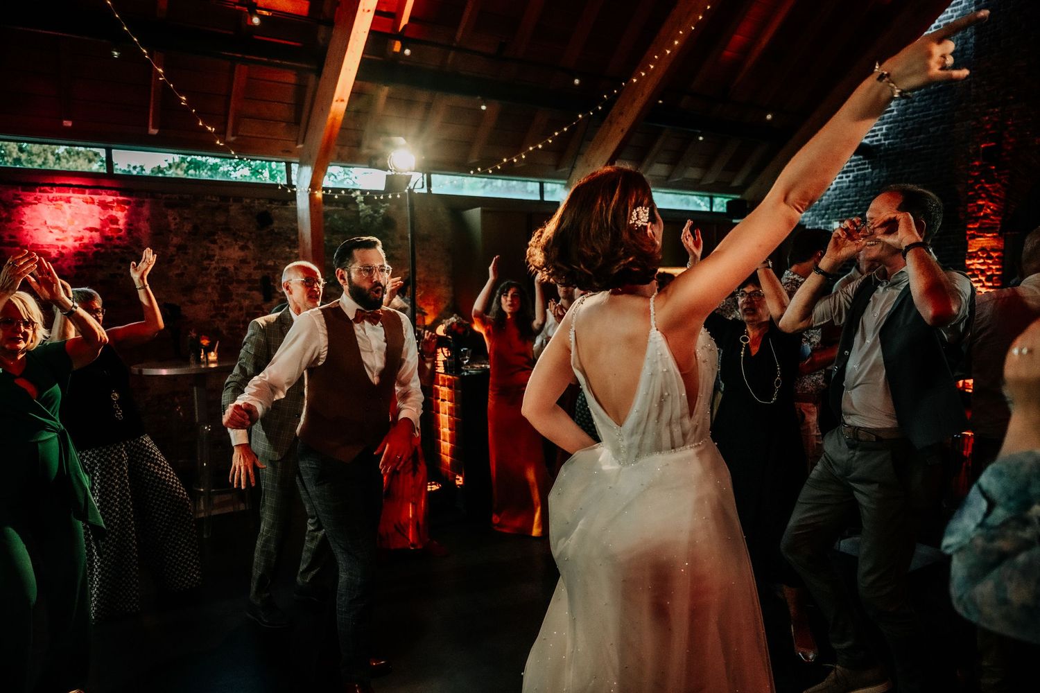 Wedding reception dance floor filled with guests celebrating under red mood lighting.