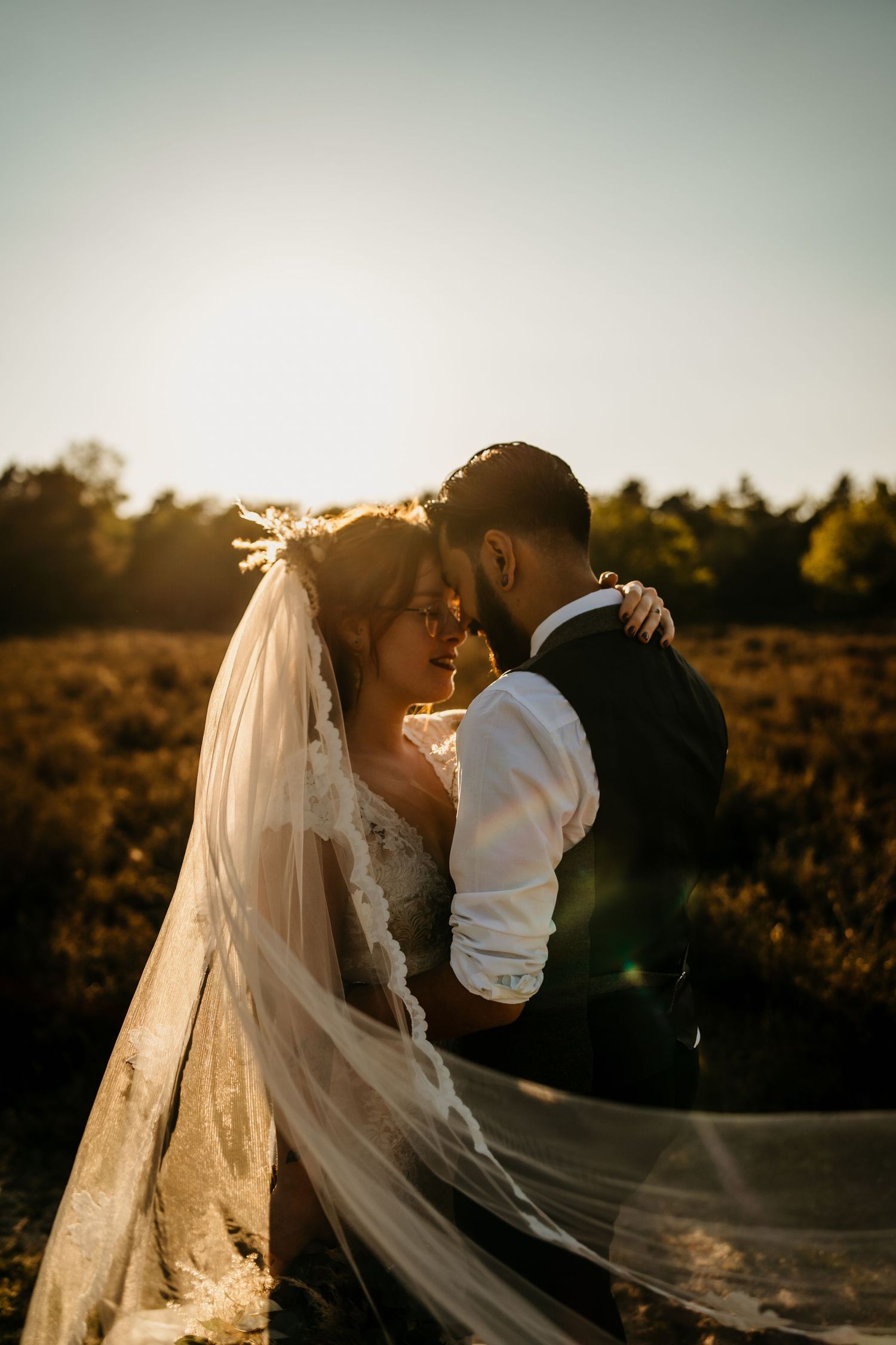 A romantic sunset portrait of newlyweds embracing with a flowing veil in golden light.
