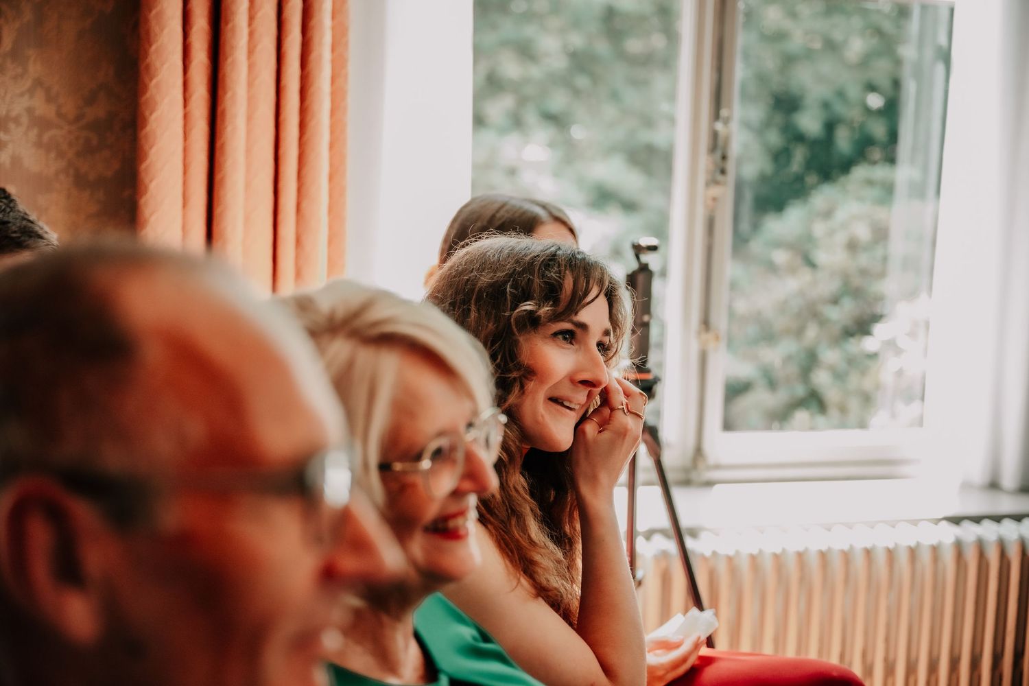 Wedding reception guests watching emotional moment through window light.