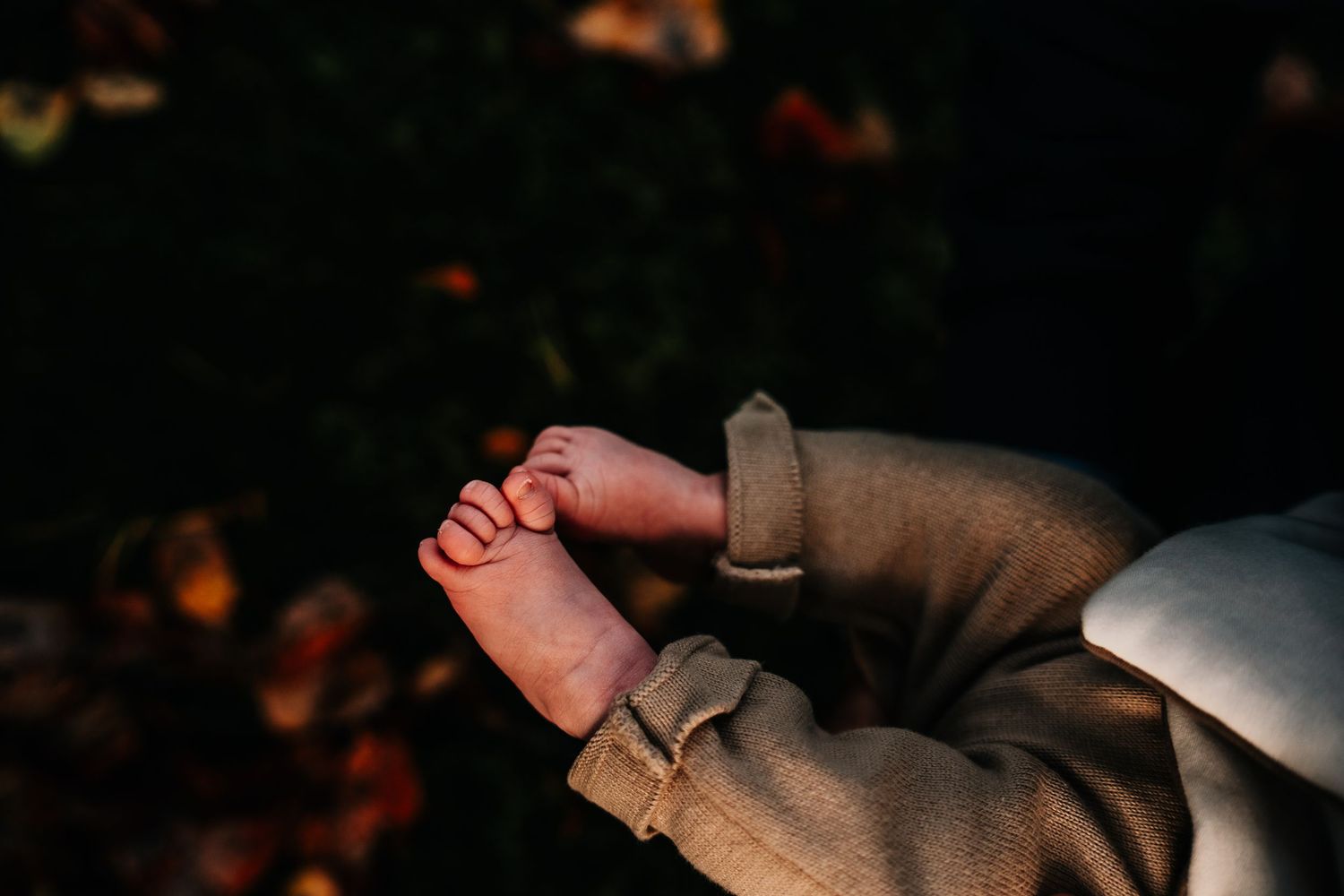 Close-up of tiny baby feet in gray onesie against dark background.