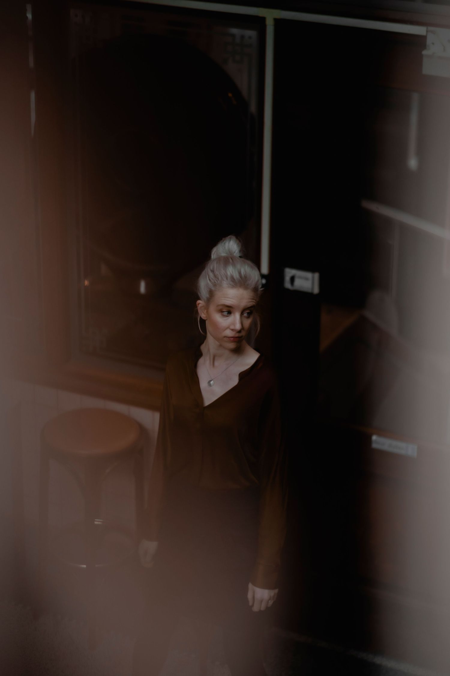 Dramatic black and white portrait shot through window blinds creating moody shadows and lines across the subject.