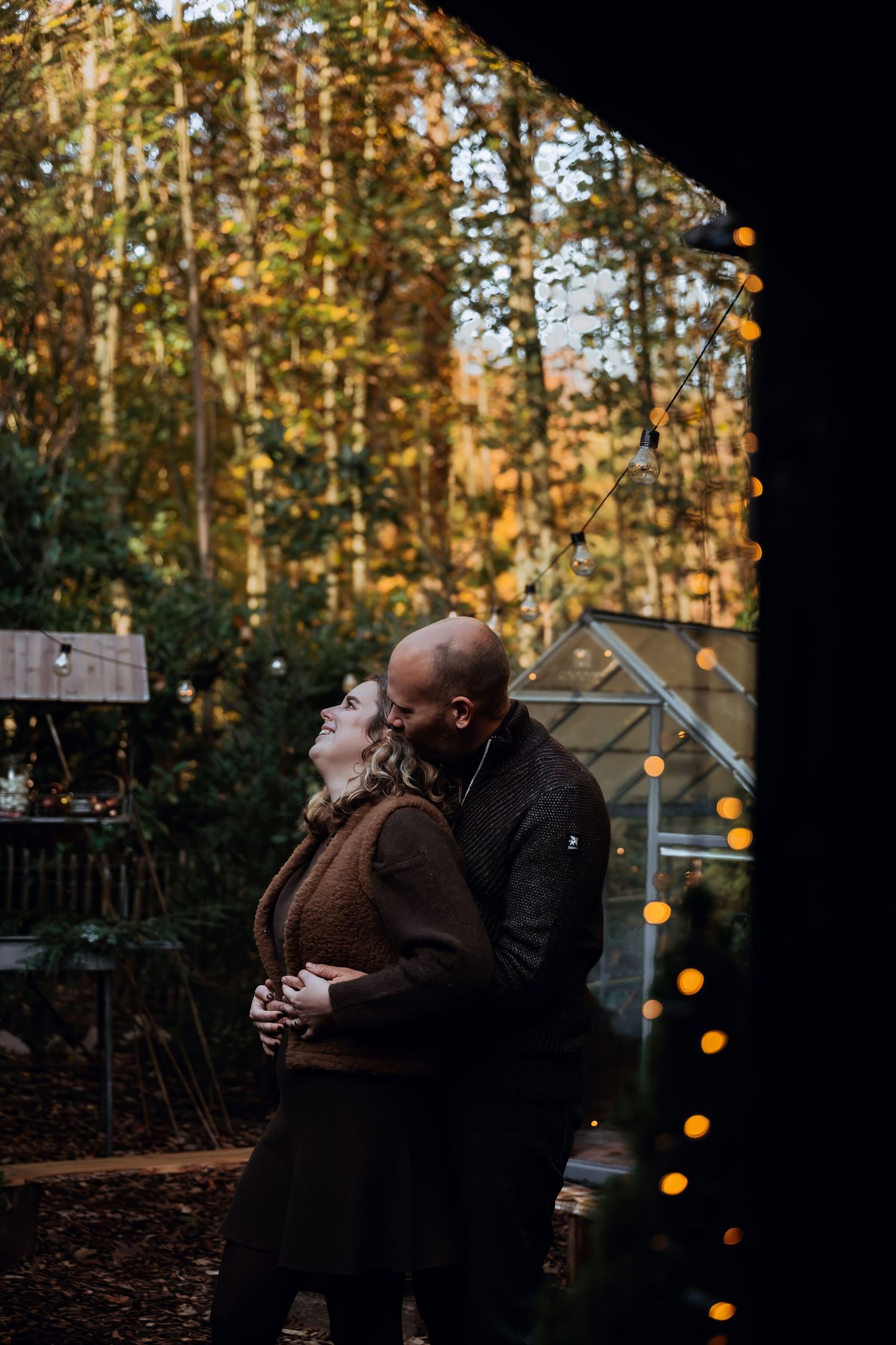 A couple shares an intimate moment at dusk in a garden setting decorated with twinkling string lights.